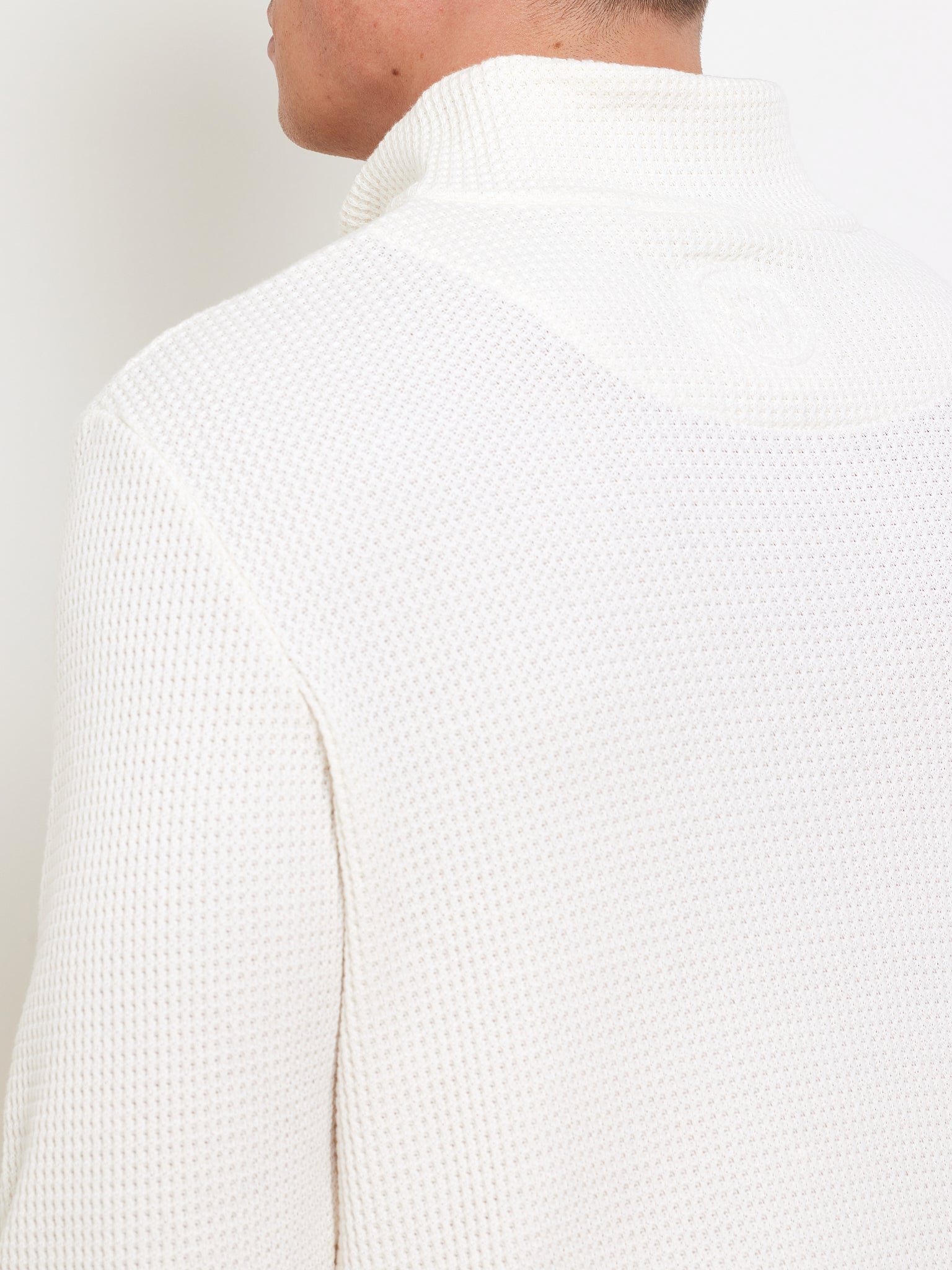 A person is wearing a textured, off-white Waffle Sweater Men by We Norwegians, made from 100% cotton with a relaxed fit. The back view highlights the intricate knit pattern against a plain white background.