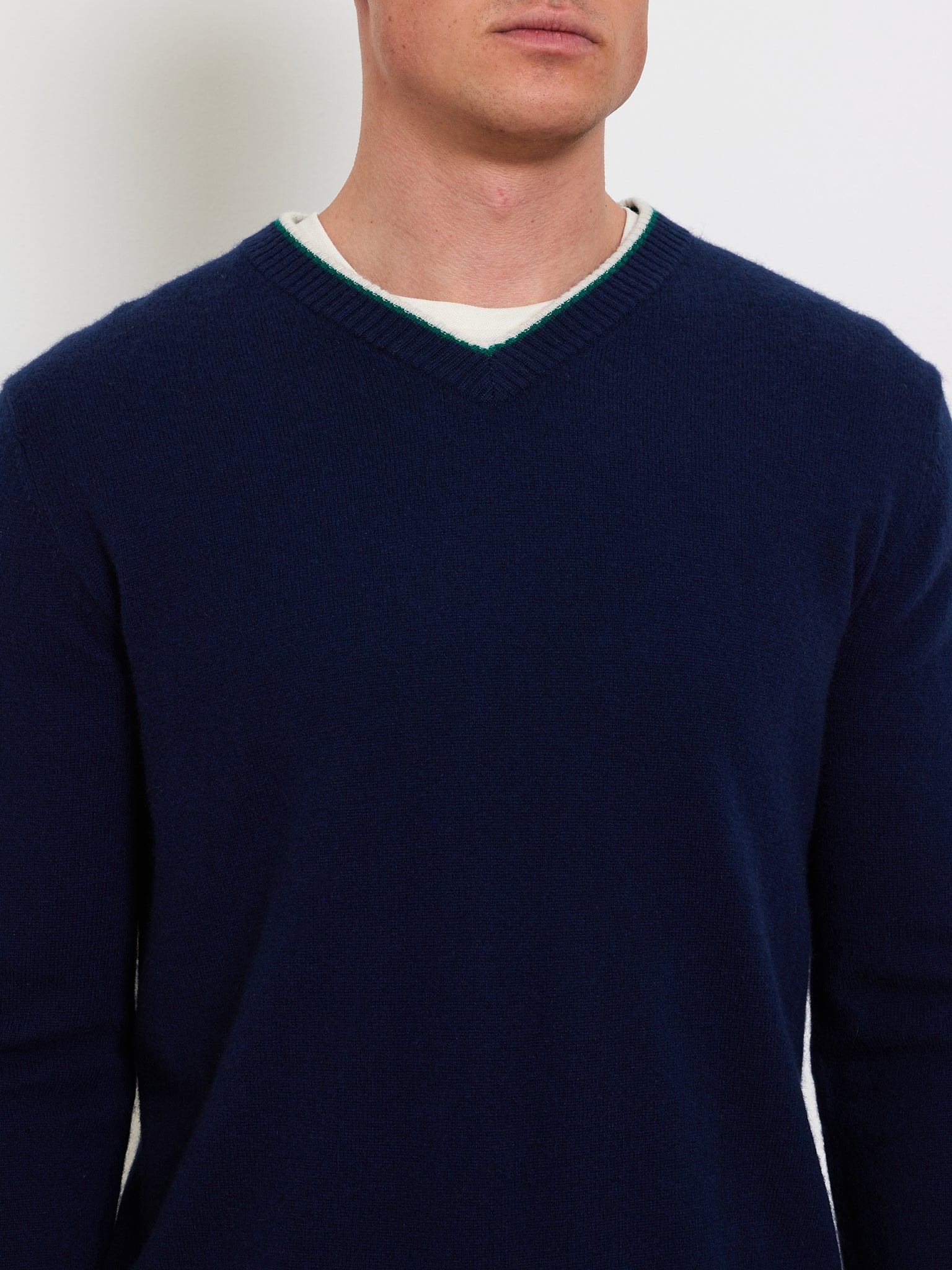 A person is wearing a Club Sweater Men by We Norwegians in navy blue over a white T-shirt, depicted from the chin down against a plain white background.