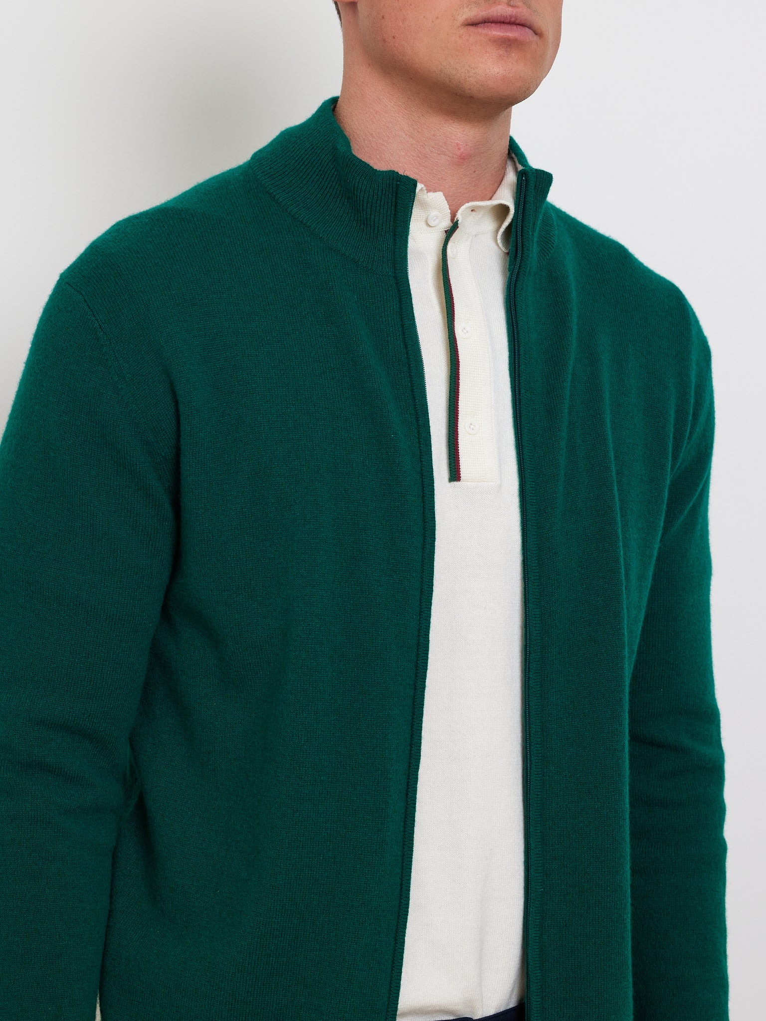 A person wearing the Club Cardigan Men by We Norwegians over a white collared shirt with stripes creates an elegant après sport look. The image highlights the torso and lower face against a plain background, exuding luxury sportswear vibes.