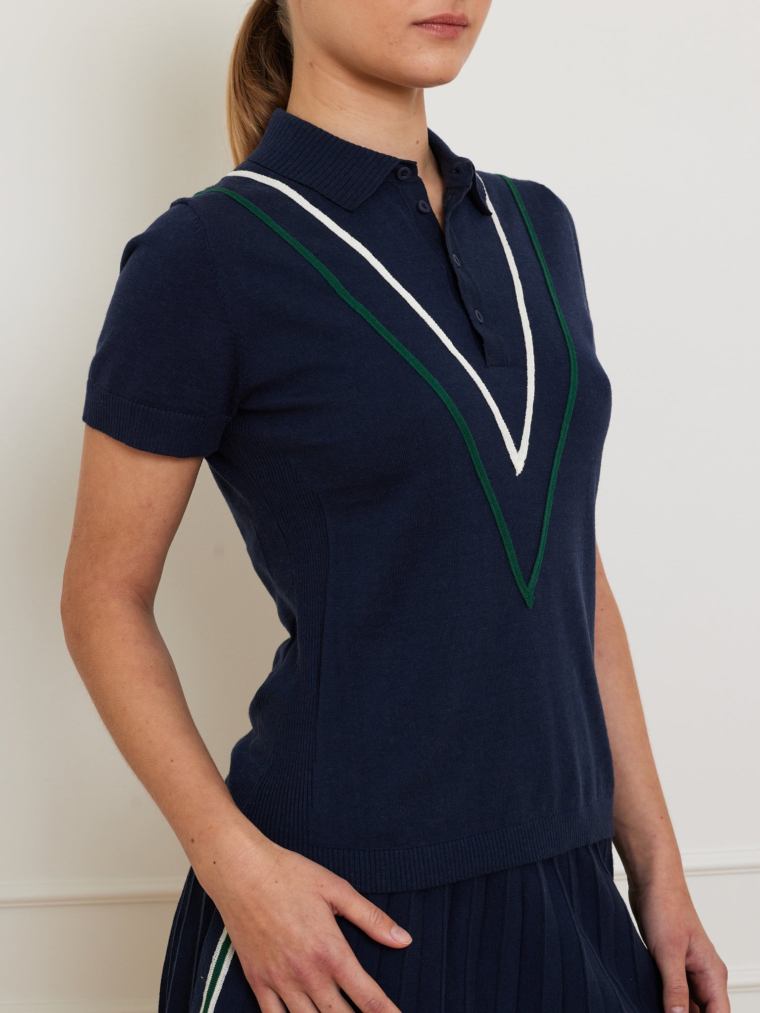 A person dons We Norwegians’ Team Chevron Polo Women, a fashionable navy blue merino cotton knit short-sleeve sweater with a white and green chevron stripe, collar, and buttons.
