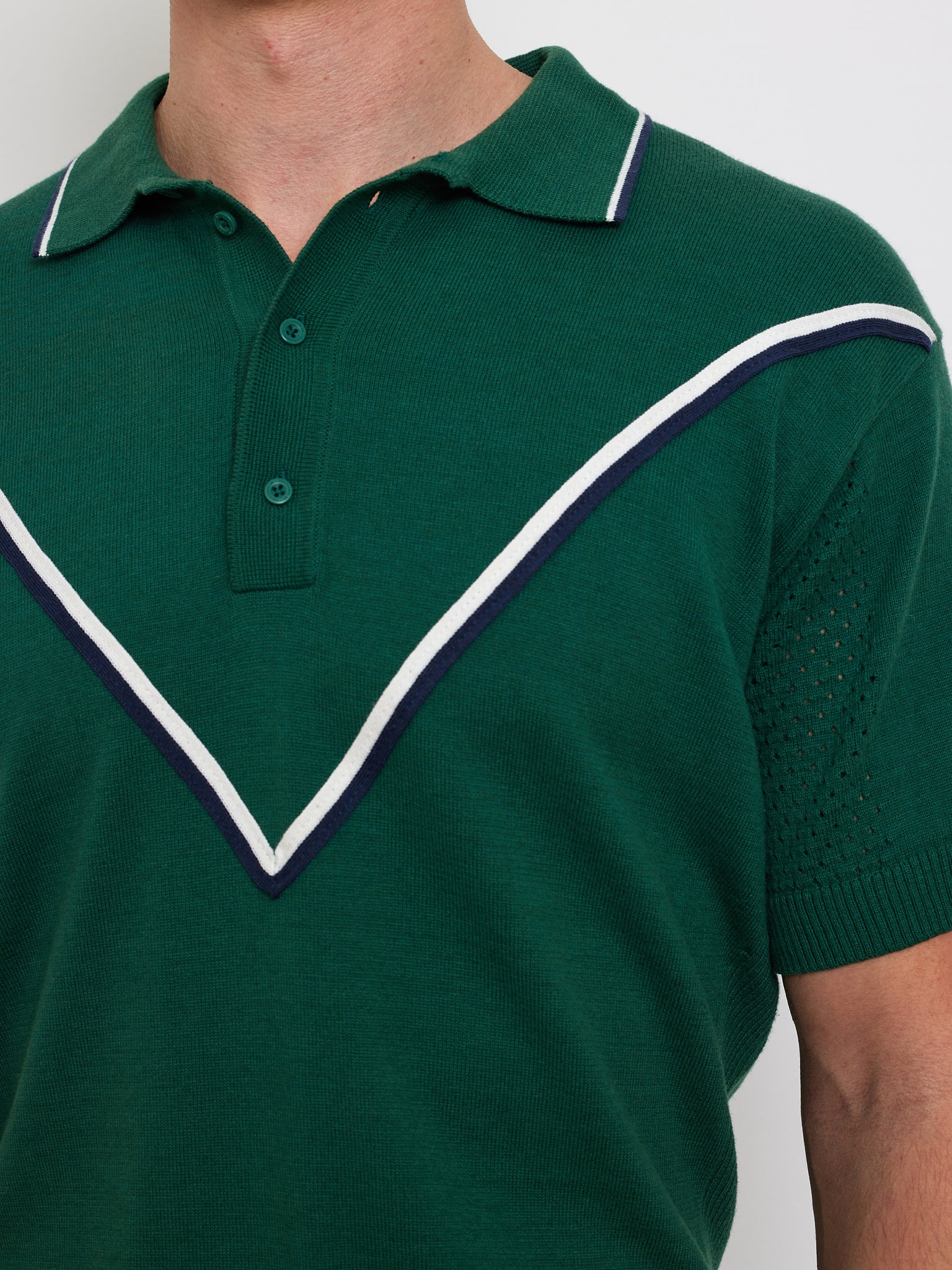 Man in a We Norwegians Team Chevron Polo, crafted from a green merino-cotton blend, showcasing an eye-catching white and navy chevron pattern on the chest and sleeves.