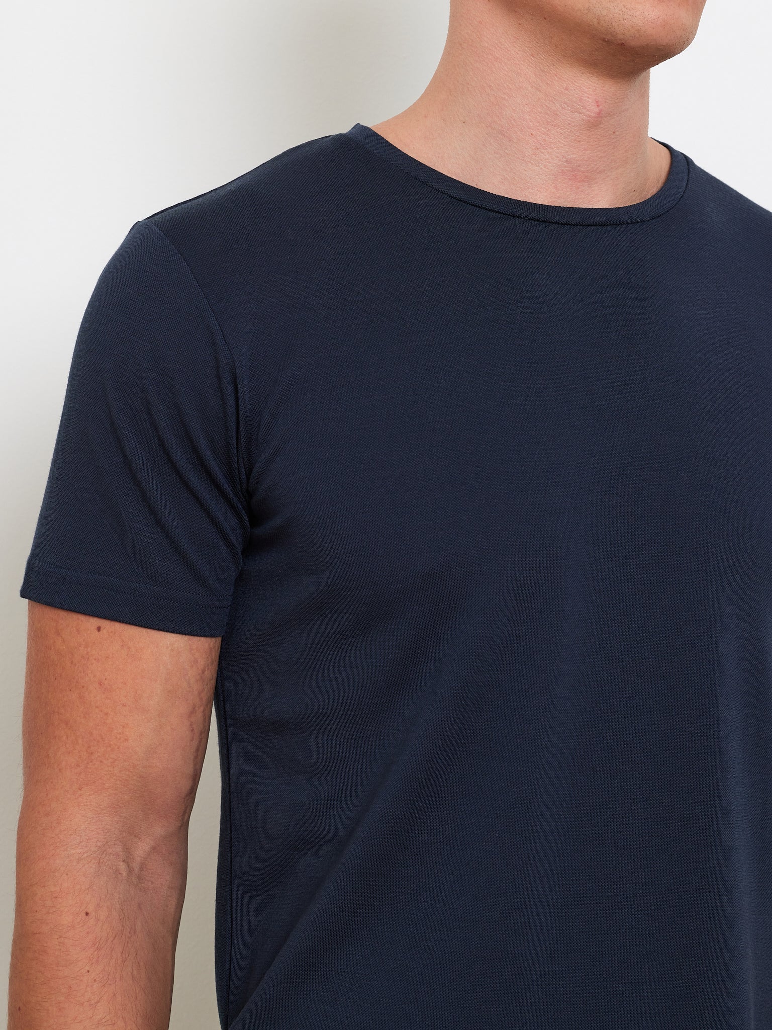 A person models the We Norwegians Medalist Piqué Tee Men from neck to waist against a light backdrop. The dark blue shirt, made from a CoolMax blend, has a round neckline and short sleeves; the head and lower body are out of view.