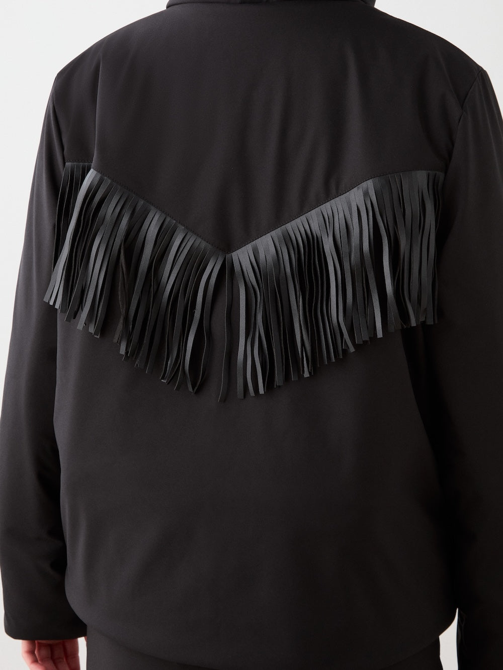 Back view of the We Norwegians Western Ski Jacket women in black, showcasing a V-shaped row of long black fringe across the upper back and shoulders for a blend of alpine style and classic flair.