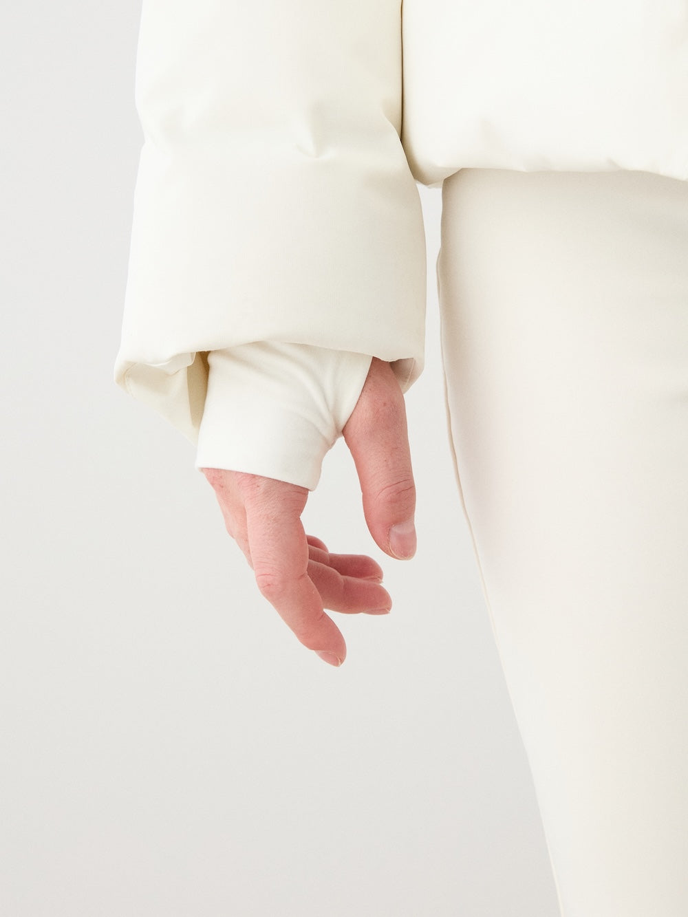 A close-up of a woman's hand and arm wearing the off-white We Norwegians Aurora Ski Jacket, with the waterproof sleeve partially covering her hand, set against a plain light background.