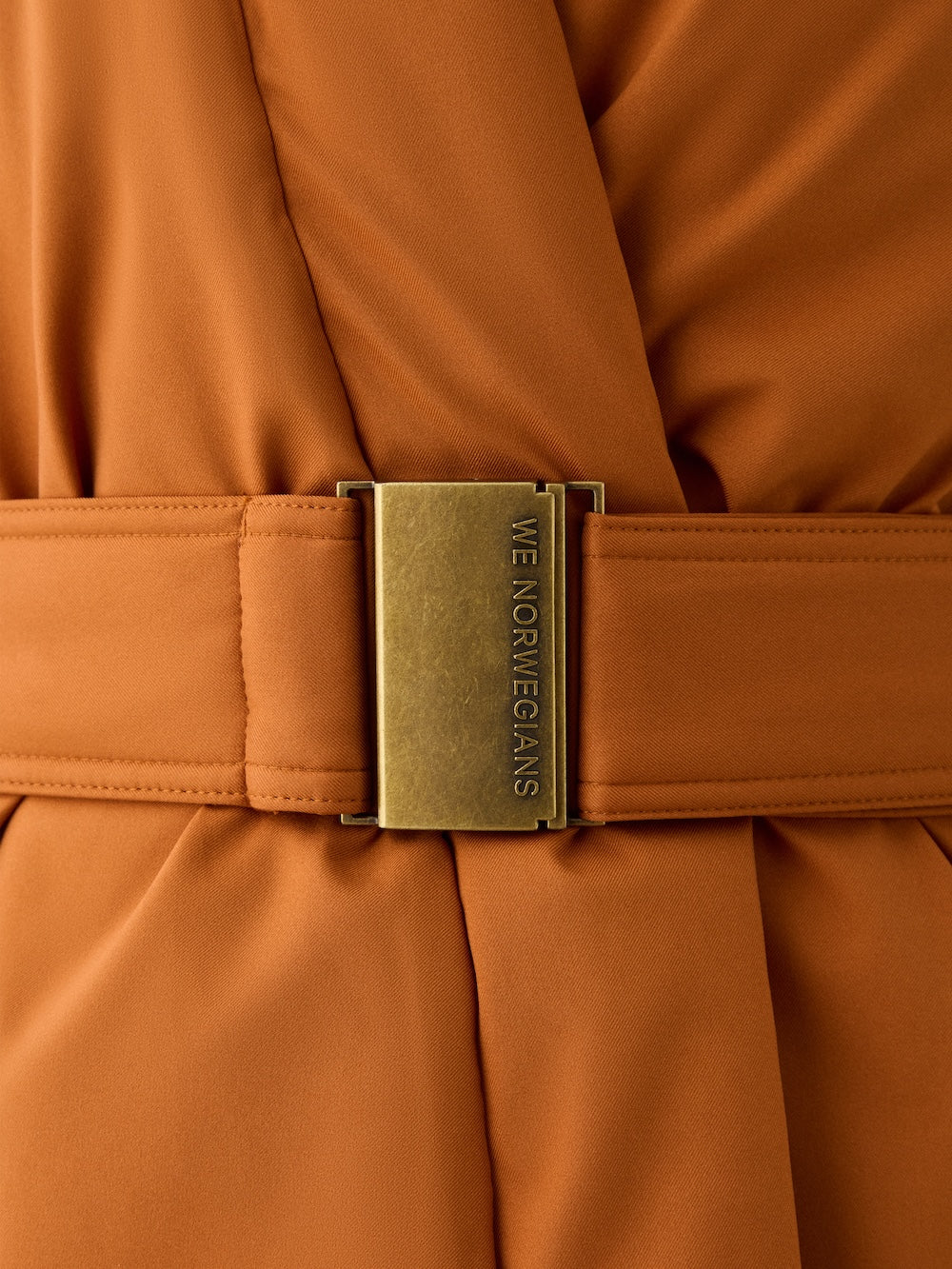 Close-up of an orange fabric belt with a large brass buckle engraved "WE NORWEGIANS," slightly gathered—an ideal accessory to pair with your favorite We Norwegians Western Vest women.