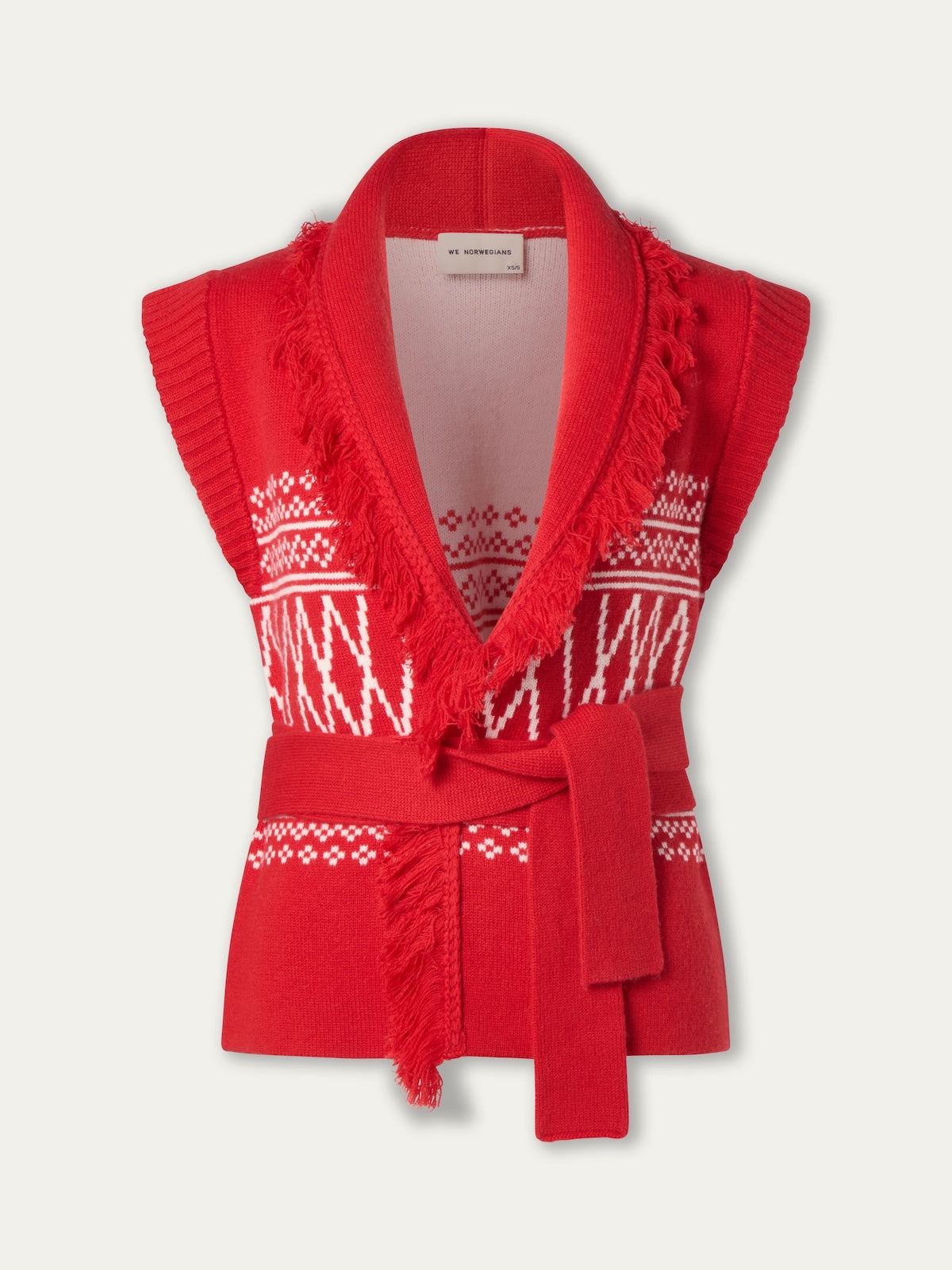The Setesdal Vest Women by We Norwegians is a sleeveless red cardigan inspired by classic Norwegian knits, featuring a shawl collar, white geometric patterns, fringe trim, and a matching waist belt.