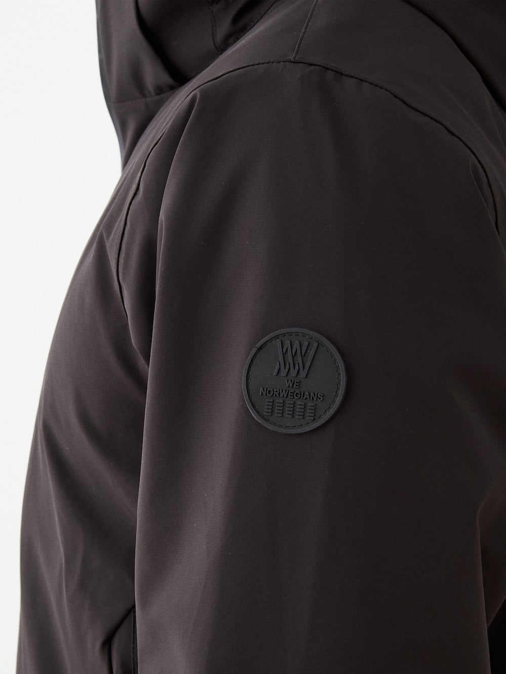 Close-up of the Hammerfest Ski Jacket men by We Norwegians shows its dark sleeve with a round black "We Norwegians" patch. The smooth, matte fabric highlights its premium quality and 4-way stretch design, ideal for skiing.