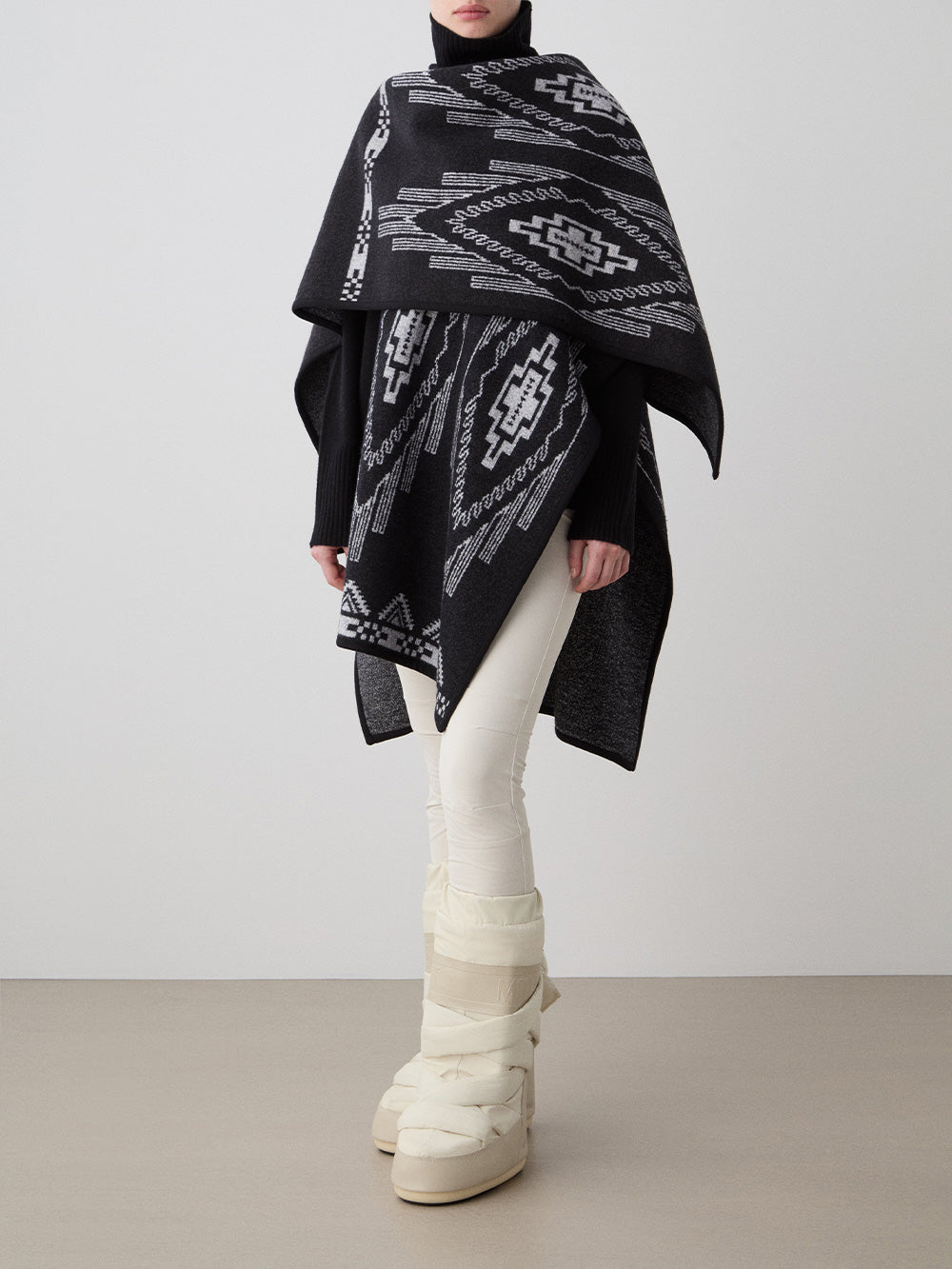 We Norwegians_FW25_Women | Model is wearing the Kautokeino poncho | Black in color with a jacquard pattern inspired by Native and Indigenous American art | Made with boiled merino wool | Photograph showing the fall and drape features of the garment against a white background