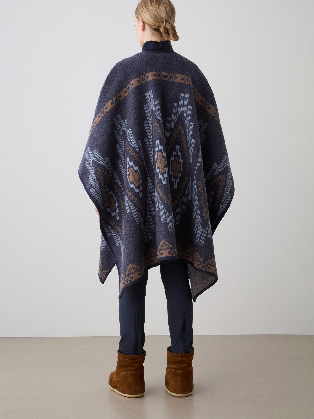 We Norwegians_FW25_Women | Model is wearing the Kautokeino poncho | Navy Blue in color with a jacquard pattern inspired by Native and Indigenous American art | Made with boiled merino wool | Back view against a white background