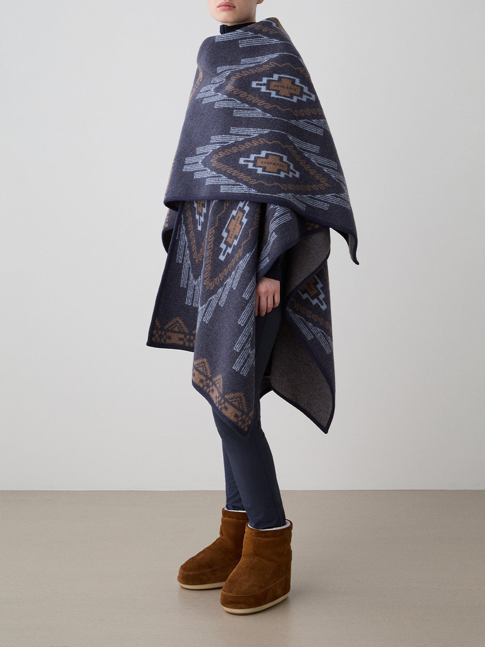 We Norwegians_FW25_Women | Model is wearing the Kautokeino poncho | Navy Blue in color with a jacquard pattern inspired by Native and Indigenous American art | Made with boiled merino wool | Photograph is showing the fall and drape features of the garment against a white background