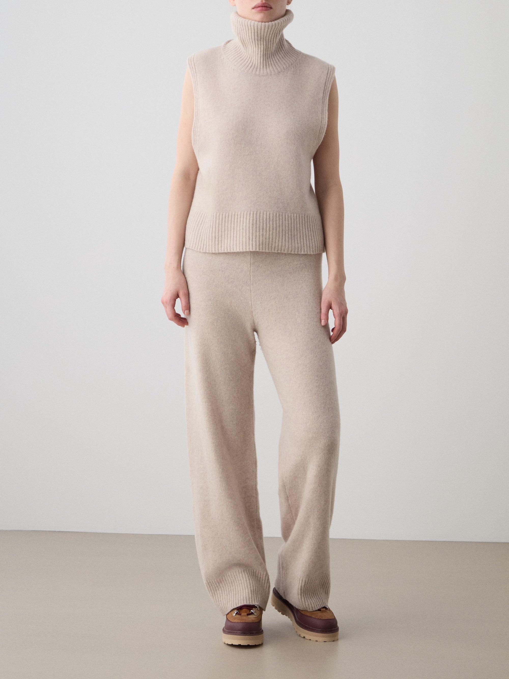Wearing the We Norwegians Geilo Vest for women with matching wide-leg knit pants, this person stands indoors by a plain wall. Brown platform shoes finish the relaxed look, arms naturally at their sides.