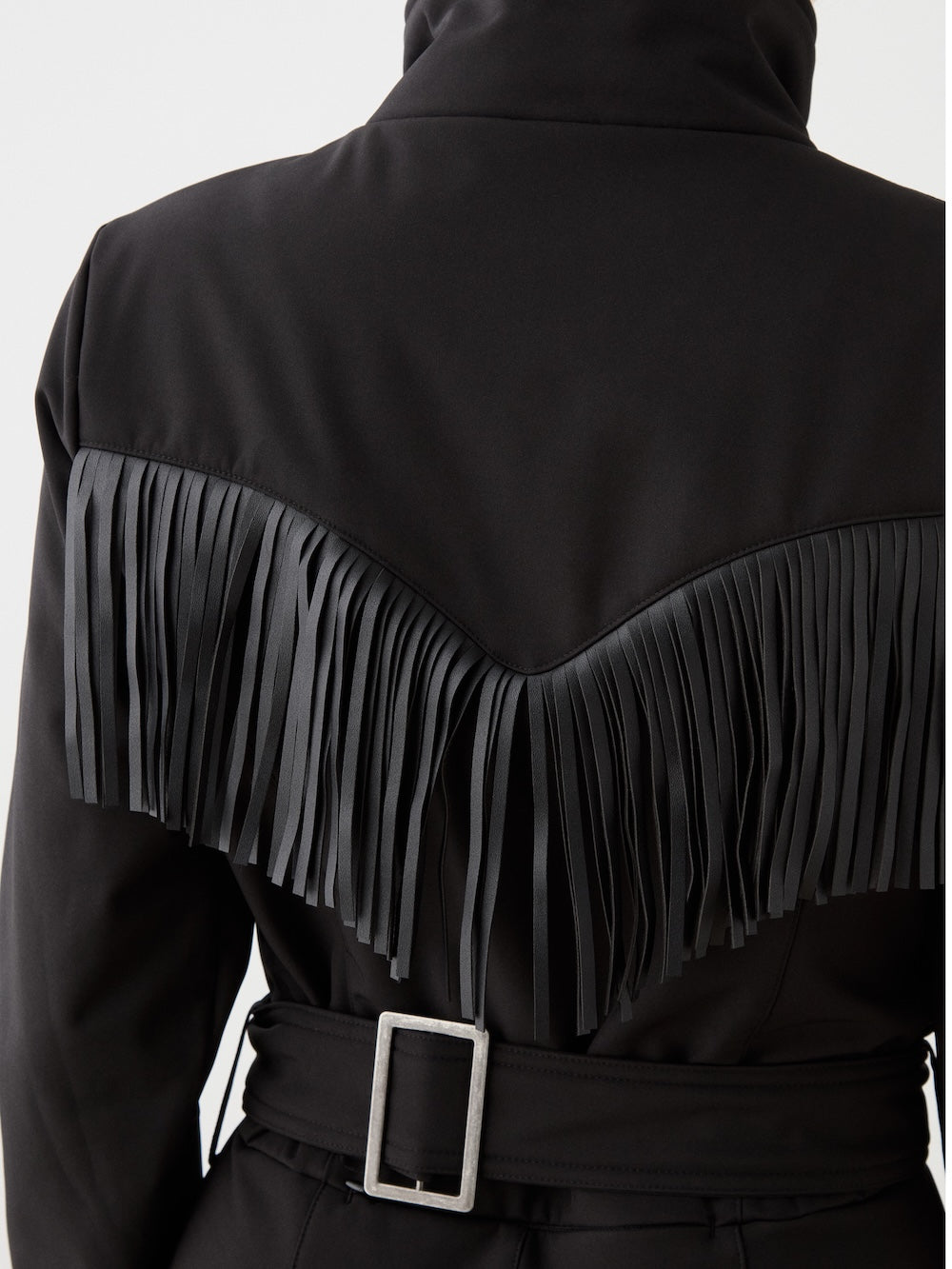 A close-up of the We Norwegians Western Ski Suit for women showcases a black belted waist with a metallic buckle and long black fringe across the shoulders—a stylish après-ski-inspired look.