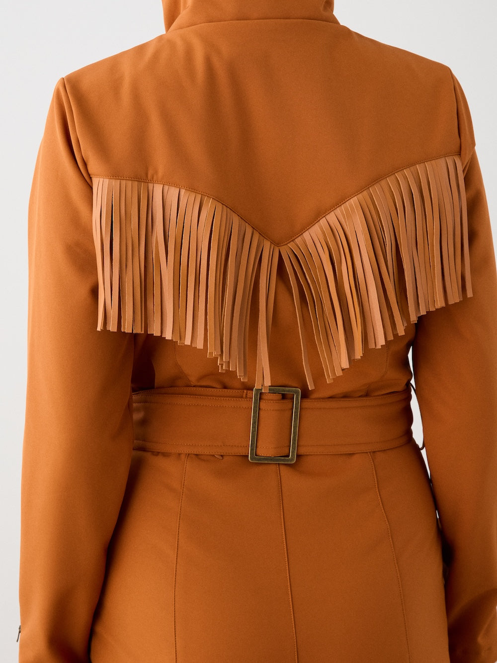 A close-up of the We Norwegians Western Ski Suit women in rust, showcasing a wide belt with a square buckle and V-shaped tan fringe across the upper back—ideal for stylish après-ski wear.