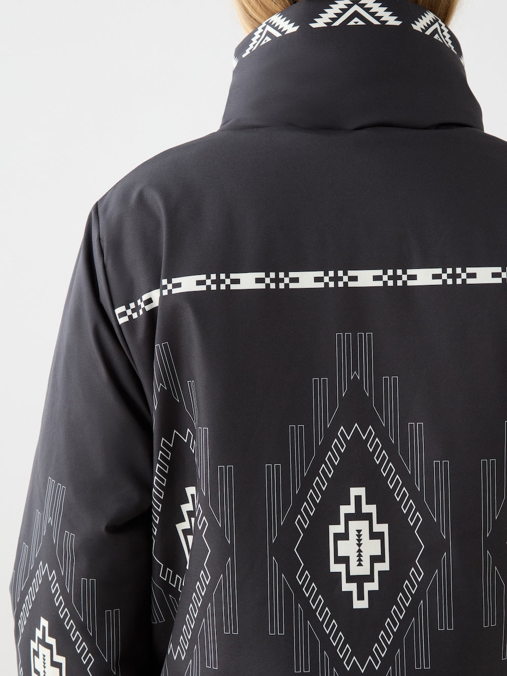 Back view of the We Norwegians Pioneer Ski Jacket women, showing its high collar and white geometric, tribal-inspired pattern on the upper back and neck. Only the upper back and neck of the wearer are visible.