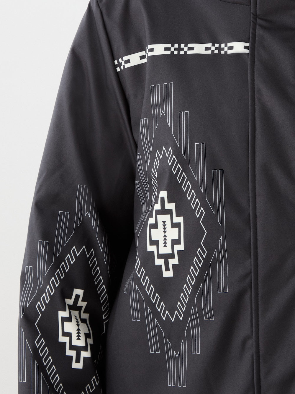 Close-up of the We Norwegians Pioneer Ski Jacket for women, showcasing white geometric and tribal-inspired patterns with diamond shapes and horizontal lines on the sleeve and shoulder for a modern yet traditional look.