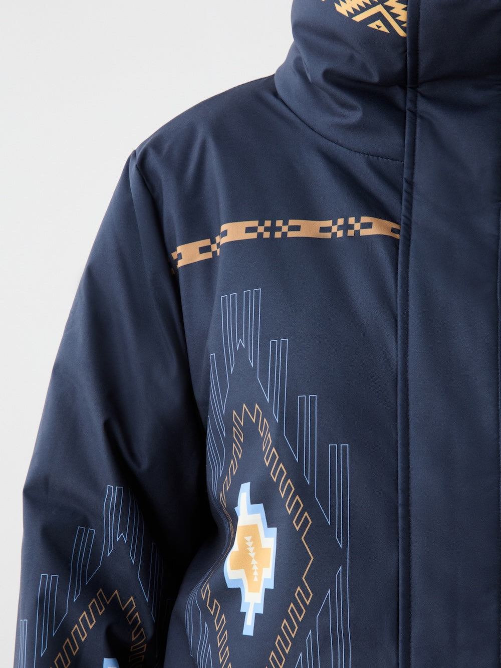 A close-up of the We Norwegians Pioneer Ski Jacket women with a high collar, displaying geometric yellow, blue, and white patterns on the chest and sleeves, inspired by Native American designs.