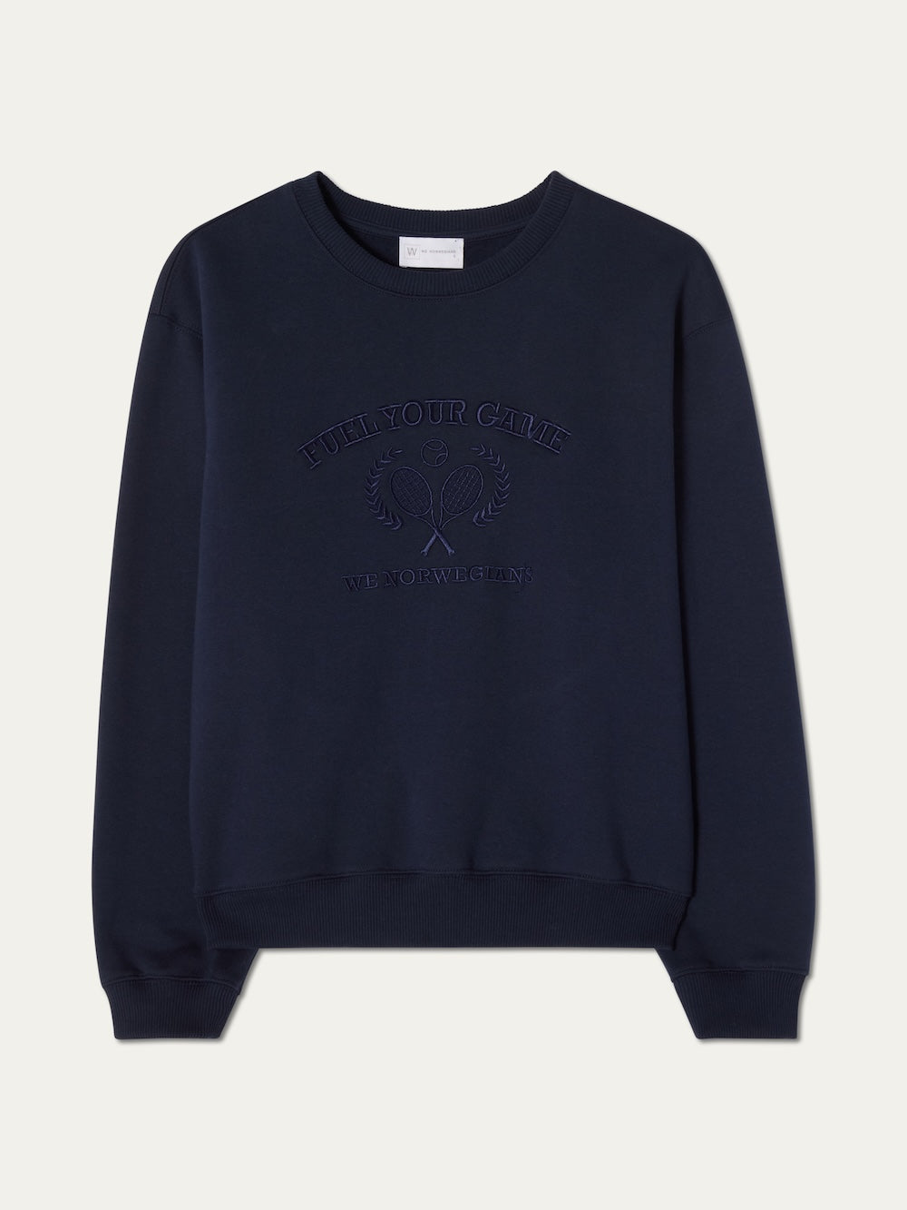 The We Norwegians Bounce Sweater Women is a navy blue crew neck with long sleeves, ribbed cuffs, and subtle embossed "FUEL YOUR GAME" text above crossed embroidered tennis rackets and "WE NOW BEGIN" below.
