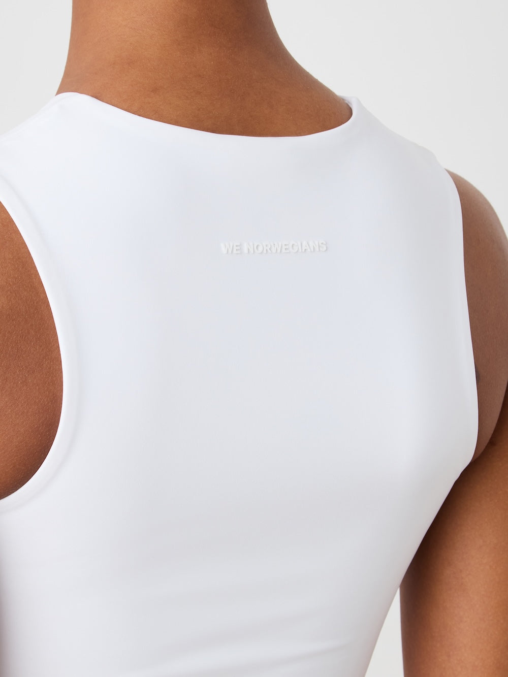 Close-up of a woman's upper back and shoulders in the We Norwegians Honor Top Women, featuring subtly embossed “WE NORWEGIANS” lettering on the high-performance white fabric.