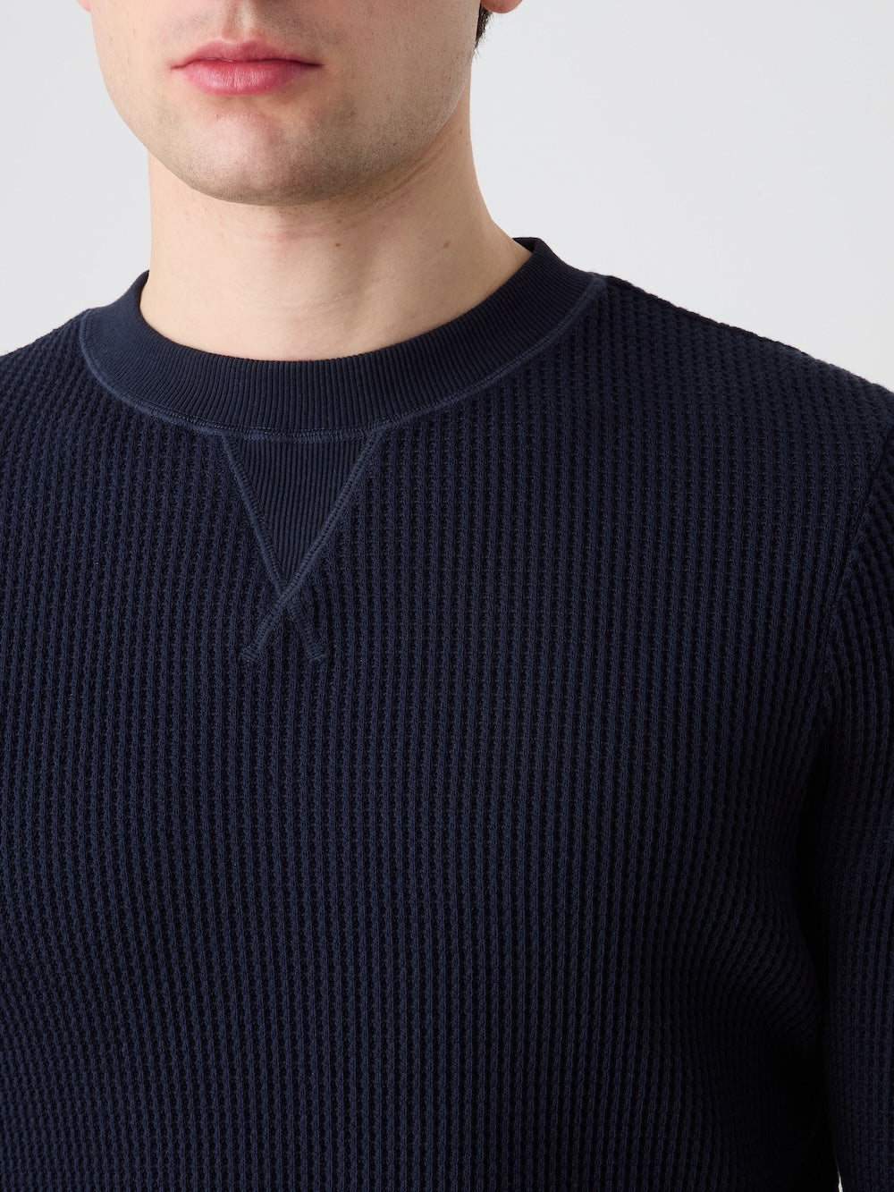 A person wearing the We Norwegians Waffle Crewneck Men sweater in dark blue, featuring a textured waffle-knit cotton design and relaxed fit, is shown from the shoulders to just above the mouth against a plain light background.