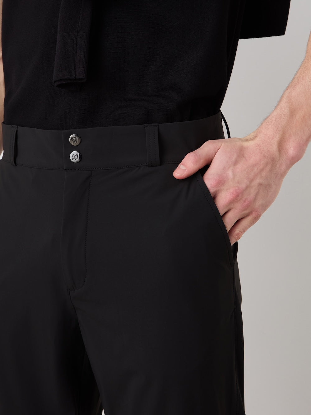 A person models the We Norwegians Albatross Pant Men, crafted from breathable performance fabric, standing with one hand in their pocket and highlighting the waistband and front buttons.