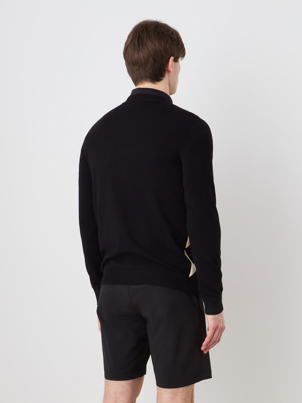 A person with short brown hair, facing away from the camera, wears the We Norwegians Fairway Sweater Men in black and black shorts, set against a plain white background.