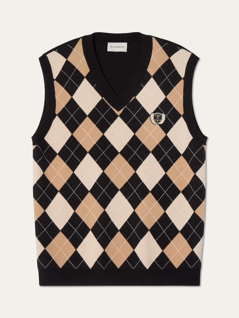 The We Norwegians Fairway Vest Men is a sleeveless, V-neck sweater vest featuring a black, beige, and white argyle knit and an embroidered crest patch on the left chest—a classic golf style with timeless appeal.