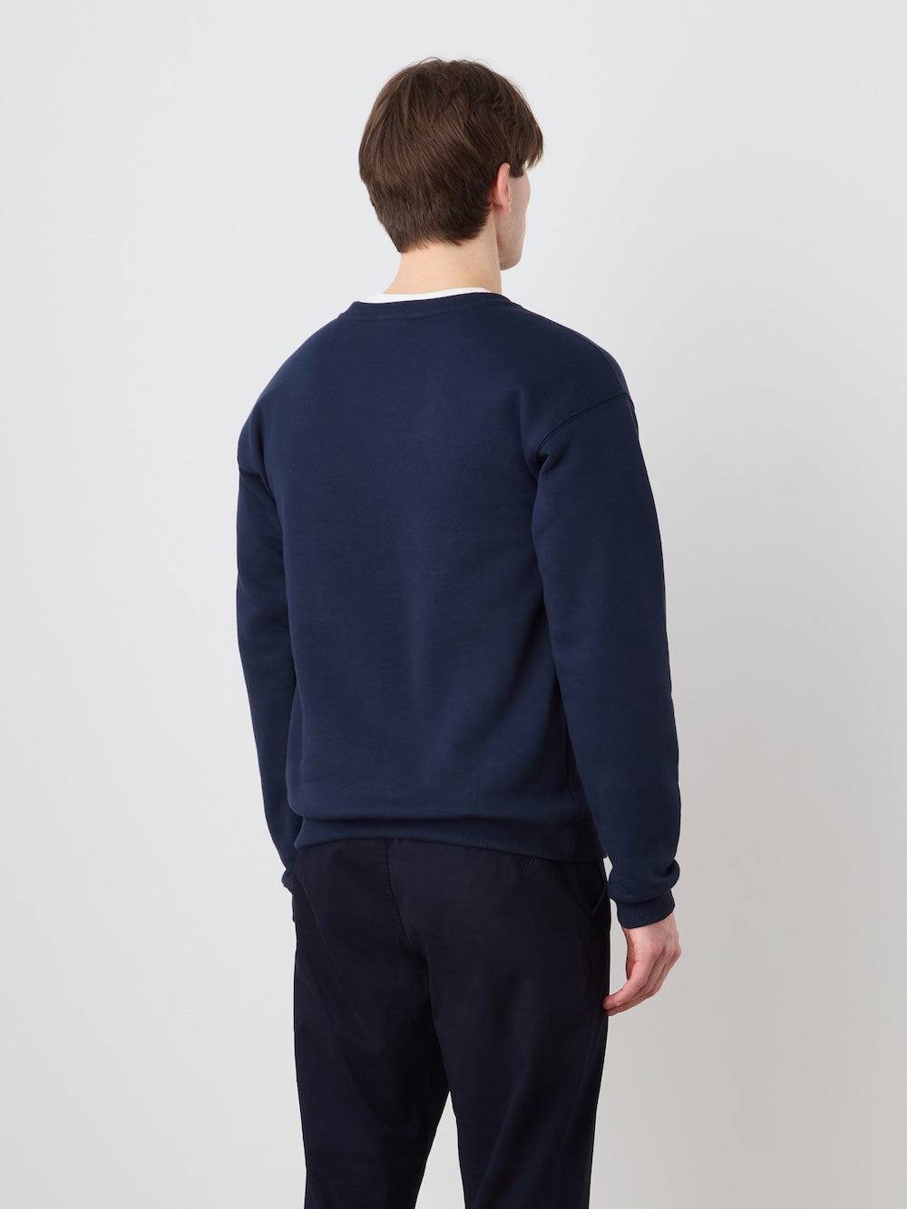 A person with short brown hair, dressed in the We Norwegians Bounce Sweater Men and matching pants in navy blue, stands facing away from the camera against a plain light background.