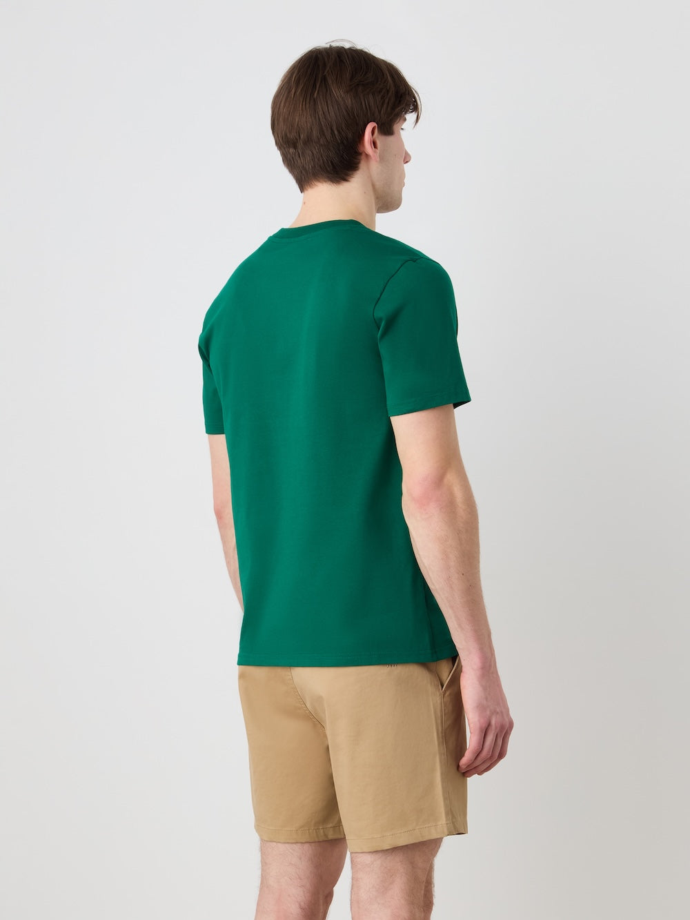 A man with brown hair stands facing away, wearing the We Norwegians Love Tee Men and tan shorts against a plain light background.