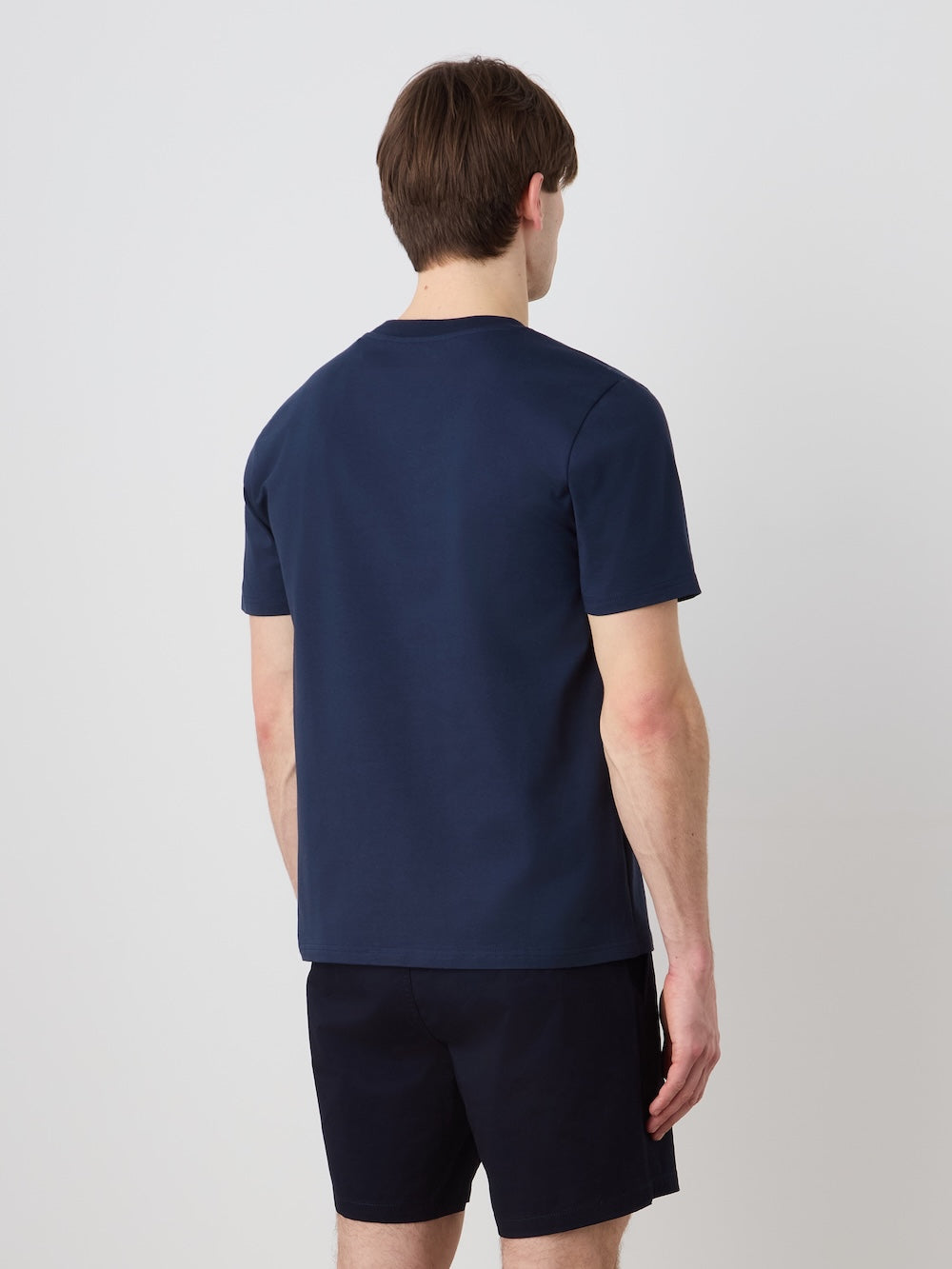 A man, seen from behind, wears the We Norwegians Love Tee Men in navy blue with matching shorts, standing before a plain light-colored background.