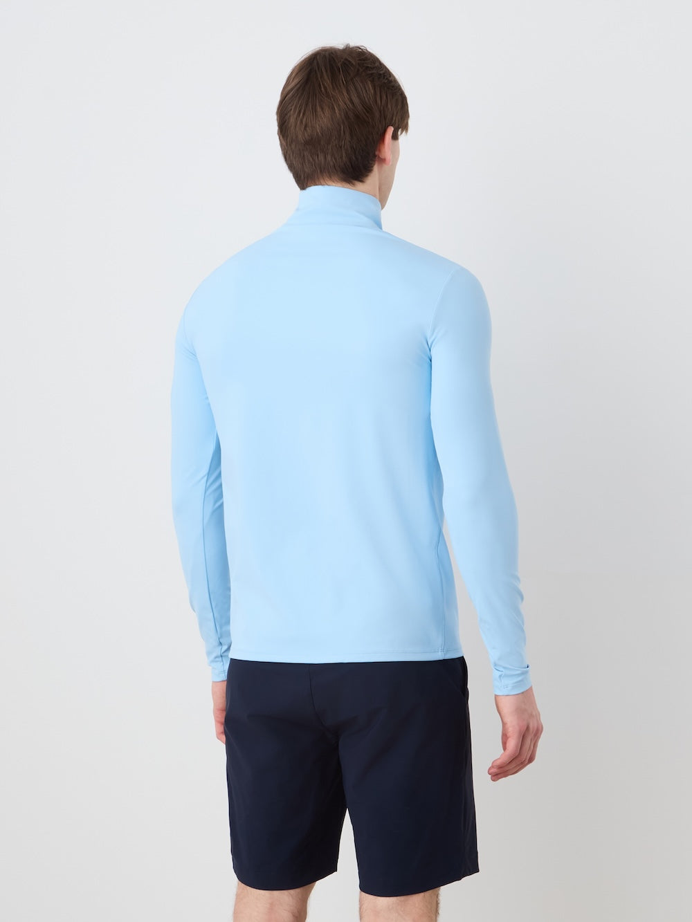 Person wearing a light blue long-sleeve shirt and dark shorts on a plain background