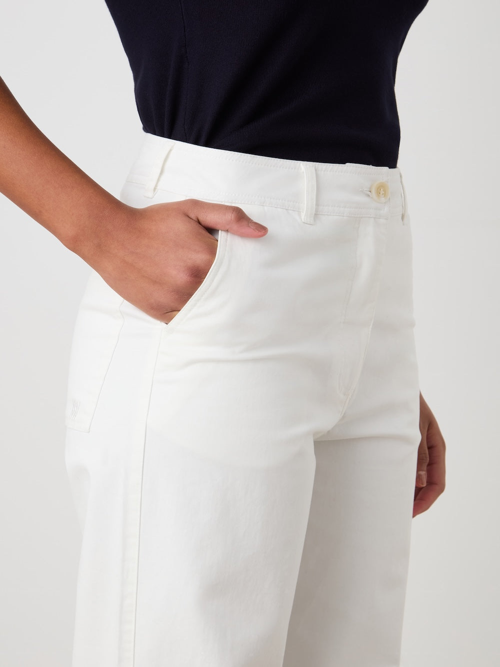 A person models the We Norwegians Sol Pant Women, vintage sailor trousers in a cotton blend, paired with a navy blue top and one hand in their pocket against a plain background.