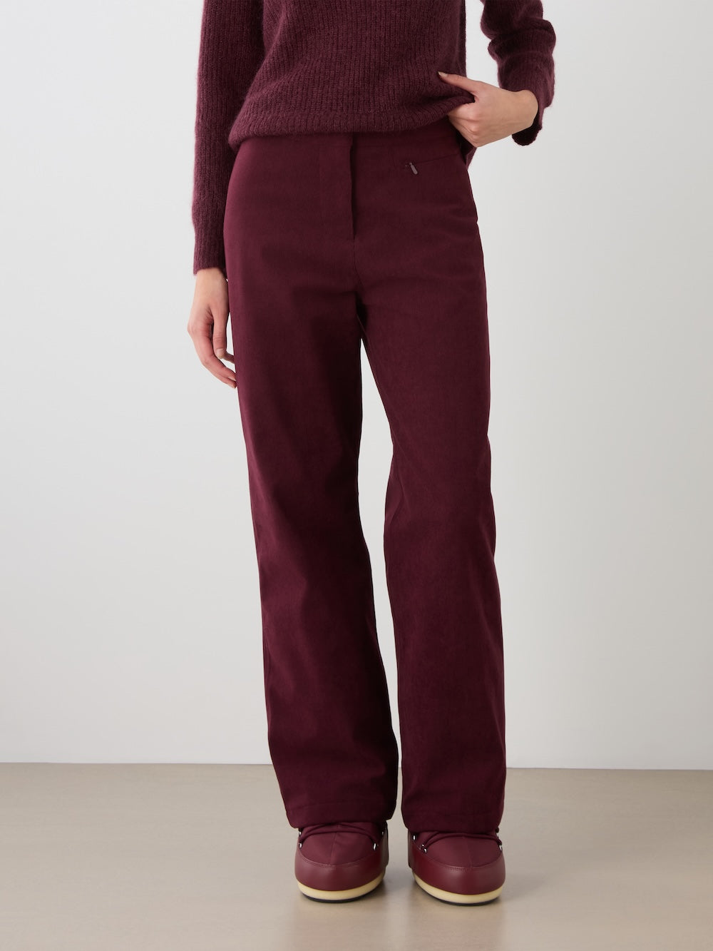 A person is shown from the waist down wearing the We Norwegians Britt Palazzo Ski Pant Women in burgundy, paired with a matching sweater and burgundy shoes, standing against a plain background.