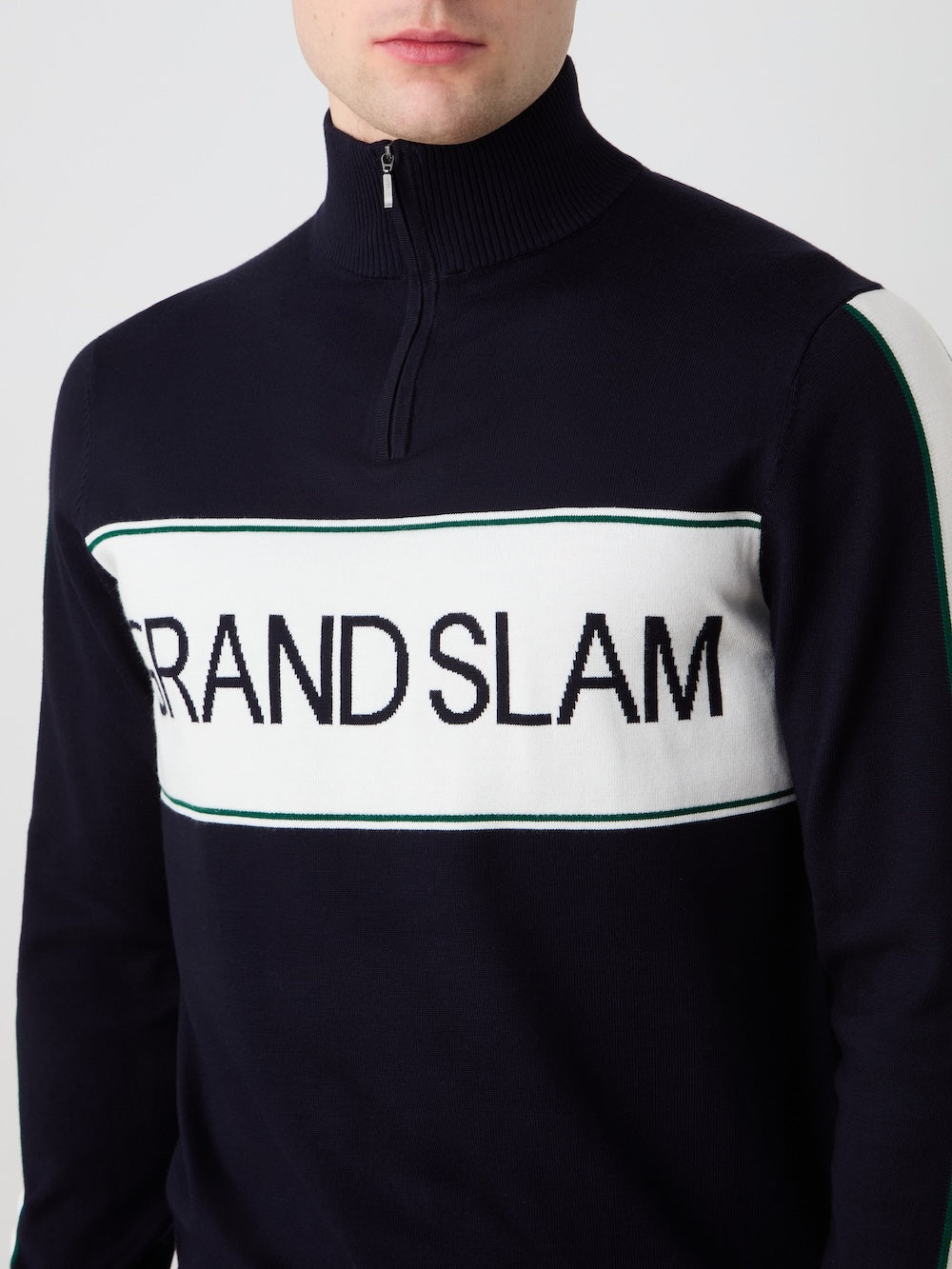 A man models the We Norwegians Grand Slam Sweater Men in navy blue, featuring "GRAND SLAM" in bold black letters on a white panel across the chest; only his lower face and upper torso are shown—a classic vintage athletic look.