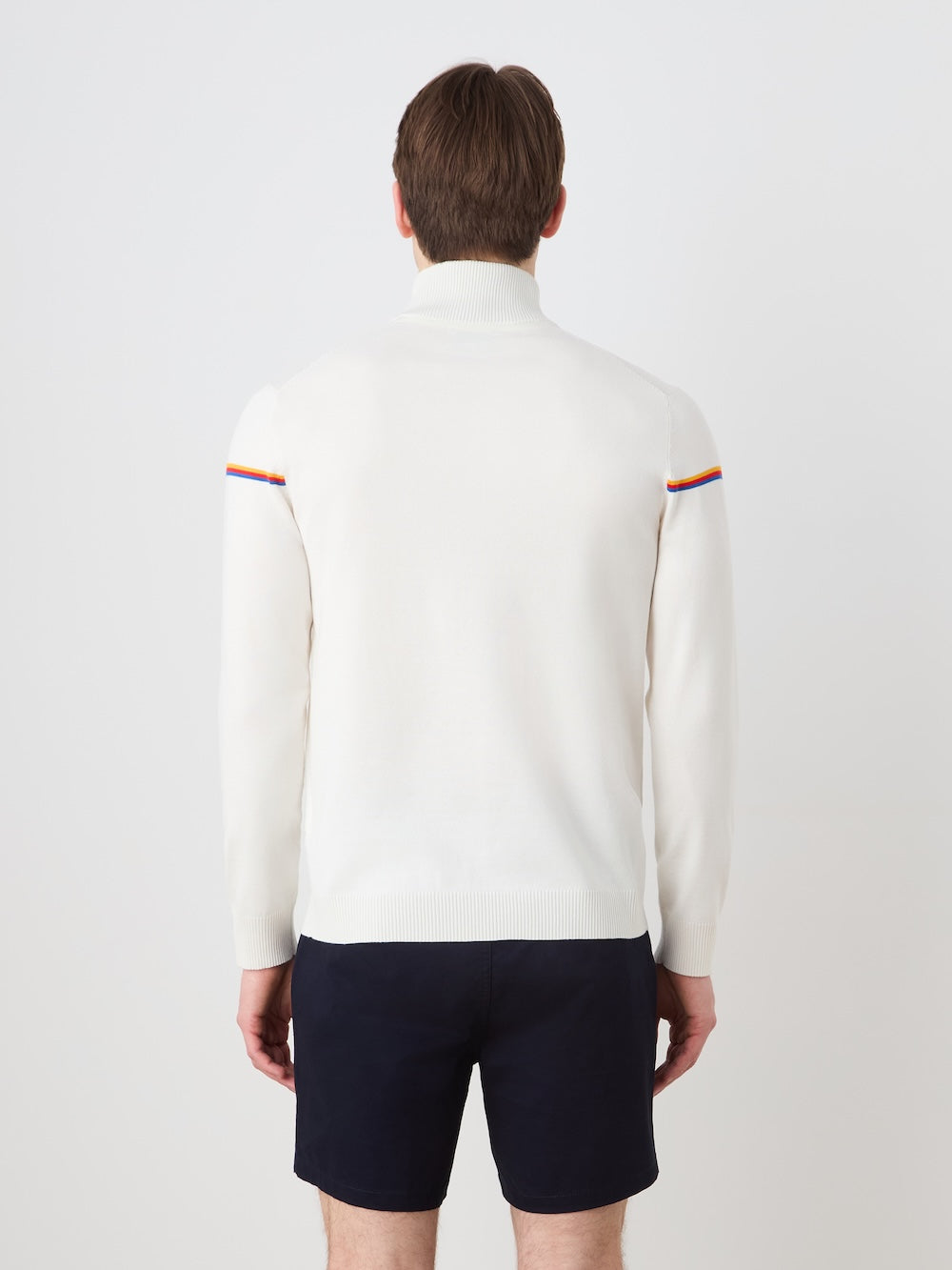 A person faces away wearing the We Norwegians Grand Slam Sweater Men, a white long-sleeve top with rainbow shoulder stripes, paired with navy shorts—showcasing classic athletic style against a plain white background.