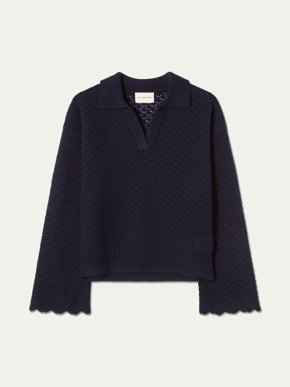 The Saeter Henley Women by We Norwegians is a navy blue long-sleeve merino wool sweater featuring a textured pointelle knit, collared V-neck Henley neckline, scalloped cuffs and hem, and a small patch pocket on one side.