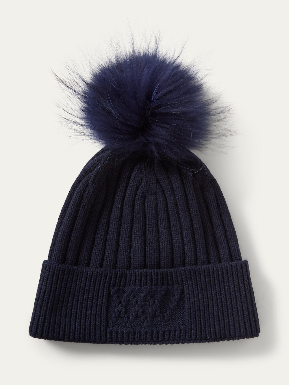 A navy blue We Norwegians Geilo PomPom Hat in a ribbed knit, finished with a matching faux fur pompom on top.
