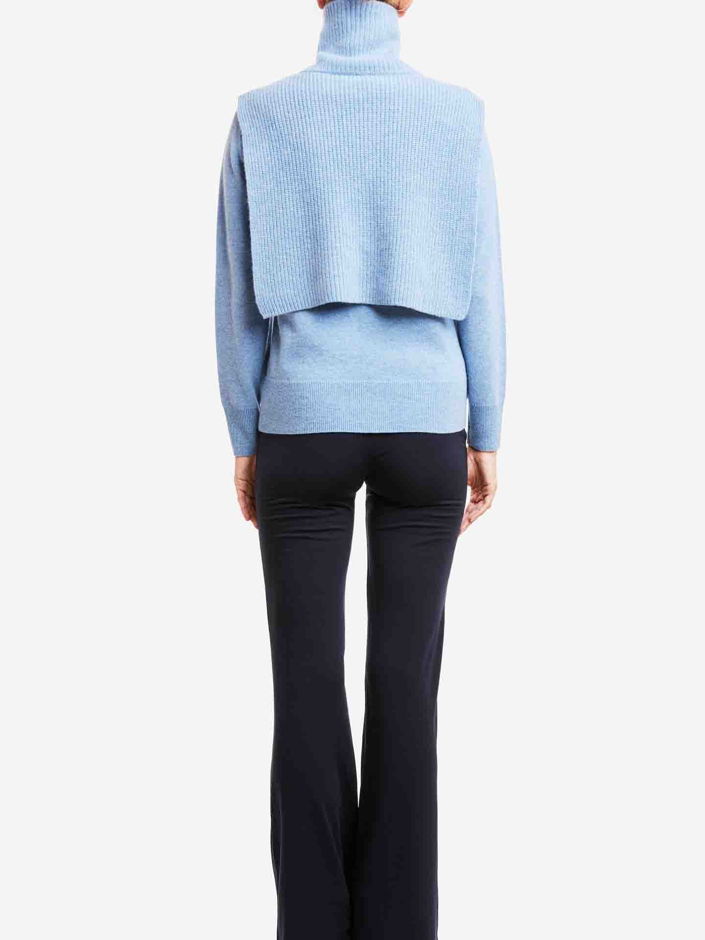 A person is shown from the back wearing a light blue turtleneck sweater with the We Norwegians Blefjell Cashmere Bib for women draped over the shoulders. They are also wearing dark flared pants against a plain white background.