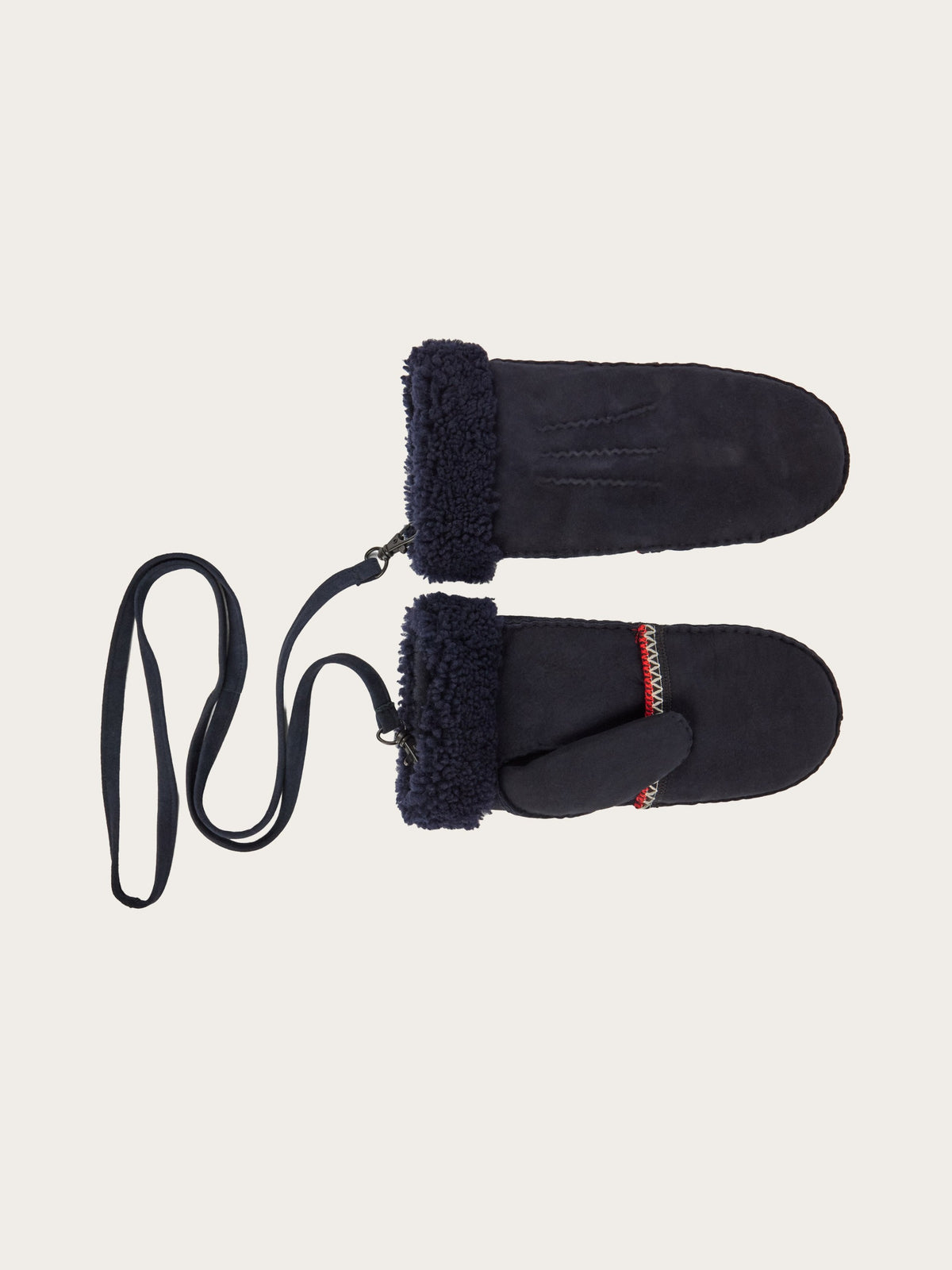 The EMU x WN Montana Mittens by We Norwegians are a cozy cold-weather essential, crafted in dark blue with fuzzy cuffs and joined by a long strap. One mitten is accented with a decorative stitched band in red and white near the wrist, showcasing classic alpine style. Shown here against a plain light background.