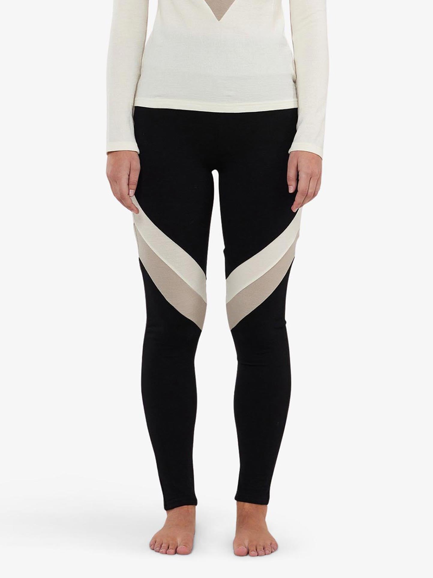 A person standing barefoot against a plain white background, wearing We Norwegians Voss ColBlock Leggings Women with white geometric patterns on the thighs and a long-sleeved merino wool shirt with a V-shaped cutout at the chest.