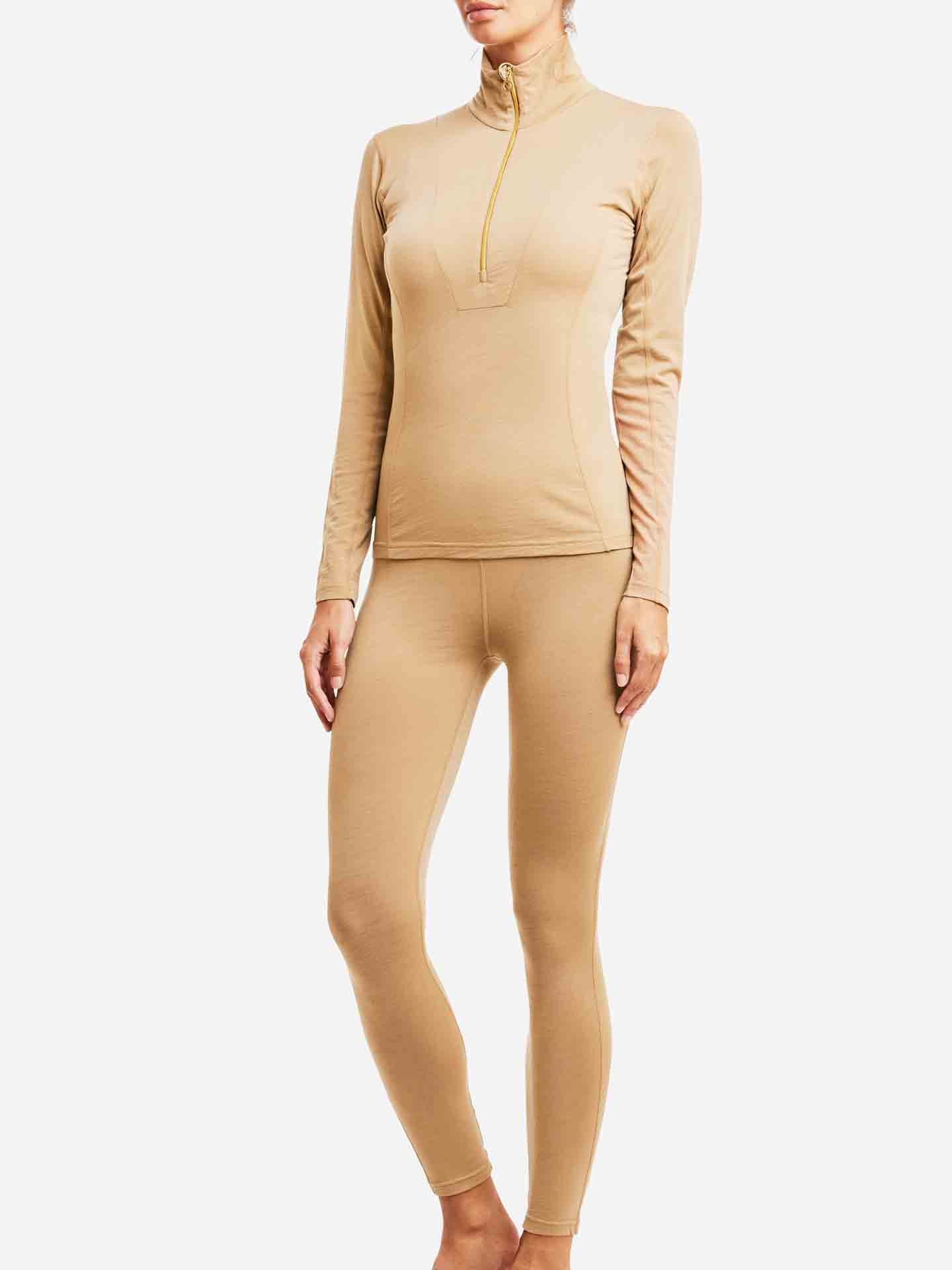 A person is wearing a fitted, long-sleeve beige top made of breathable fabric with a quarter-zip collar and matching Sno Merino Leggings for women by We Norwegians. They are posing against a plain white background. The person's face is not visible.