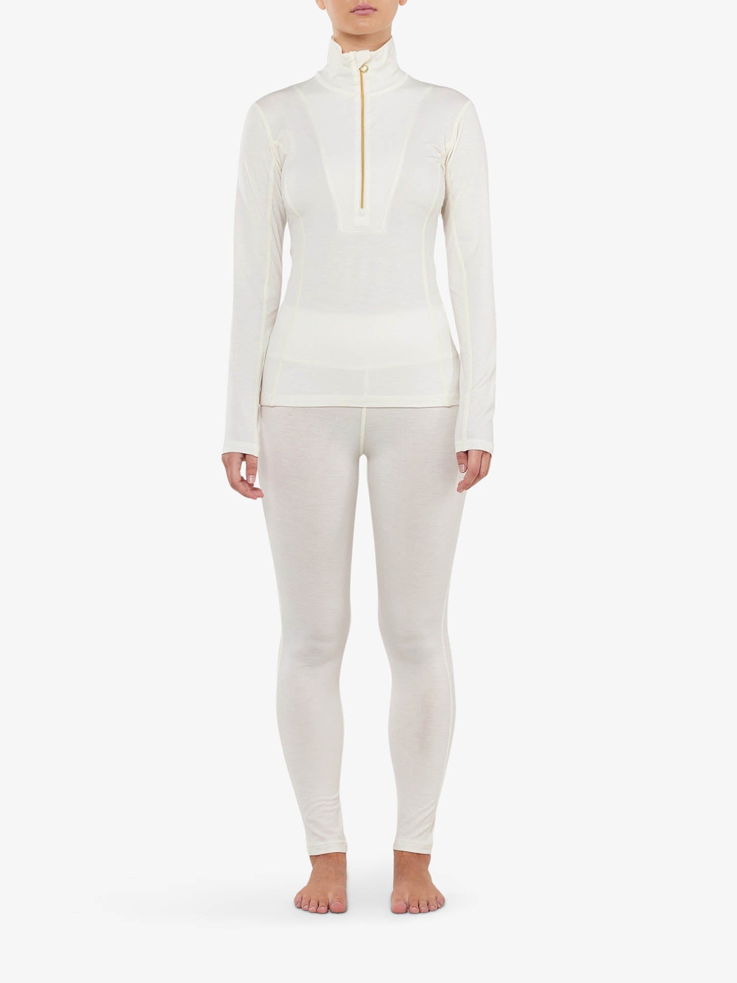 A person wearing a white, long-sleeve high-neck top with a front zipper and matching white We Norwegians Sno Merino Leggings Women. The Scandinavian luxury base-layers are form-fitting and the person is standing on a white background, barefoot, with arms relaxed at their sides.