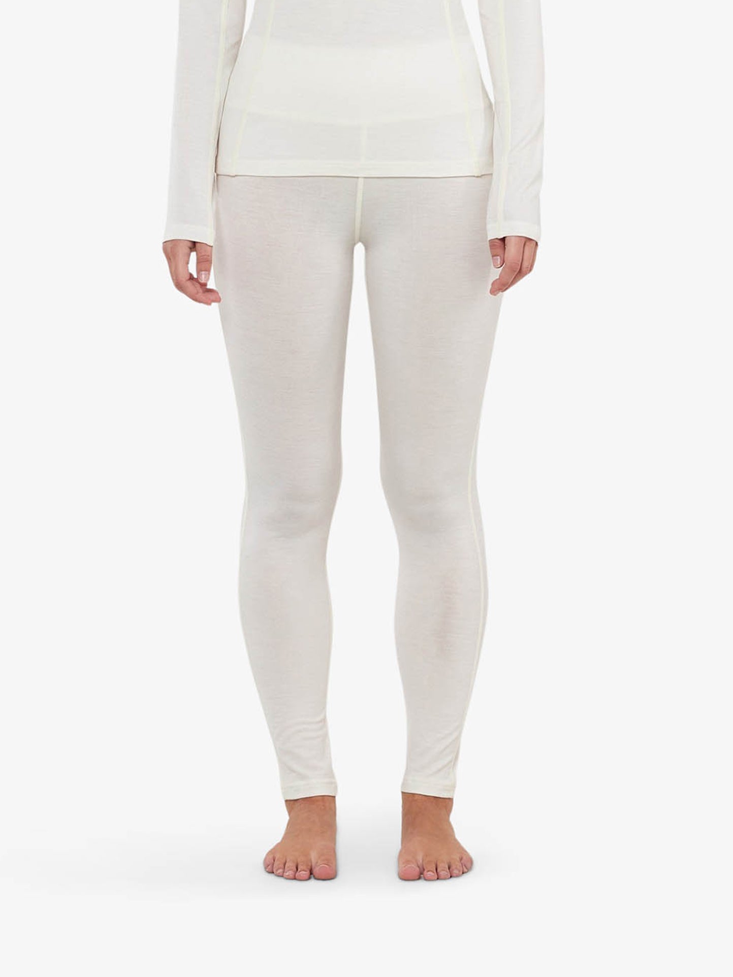 A person is standing barefoot against a plain, white background, wearing Sno Merino Leggings for women and a matching top, crafted from superfine merino wool by We Norwegians. Their arms are relaxed at their sides. The image shows only the body from the neck down, showcasing Scandinavian luxury base-layers.