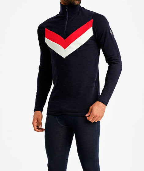 A person wearing the We Norwegians Voss Chevron Zipup Men, featuring a stylish black design with a white and red chevron pattern on the chest. Made from superfine Merino wool, this top also boasts a quarter-zip collar. The individual complements the look with black form-fitting athletic pants, exuding retro vibes against a plain white background.