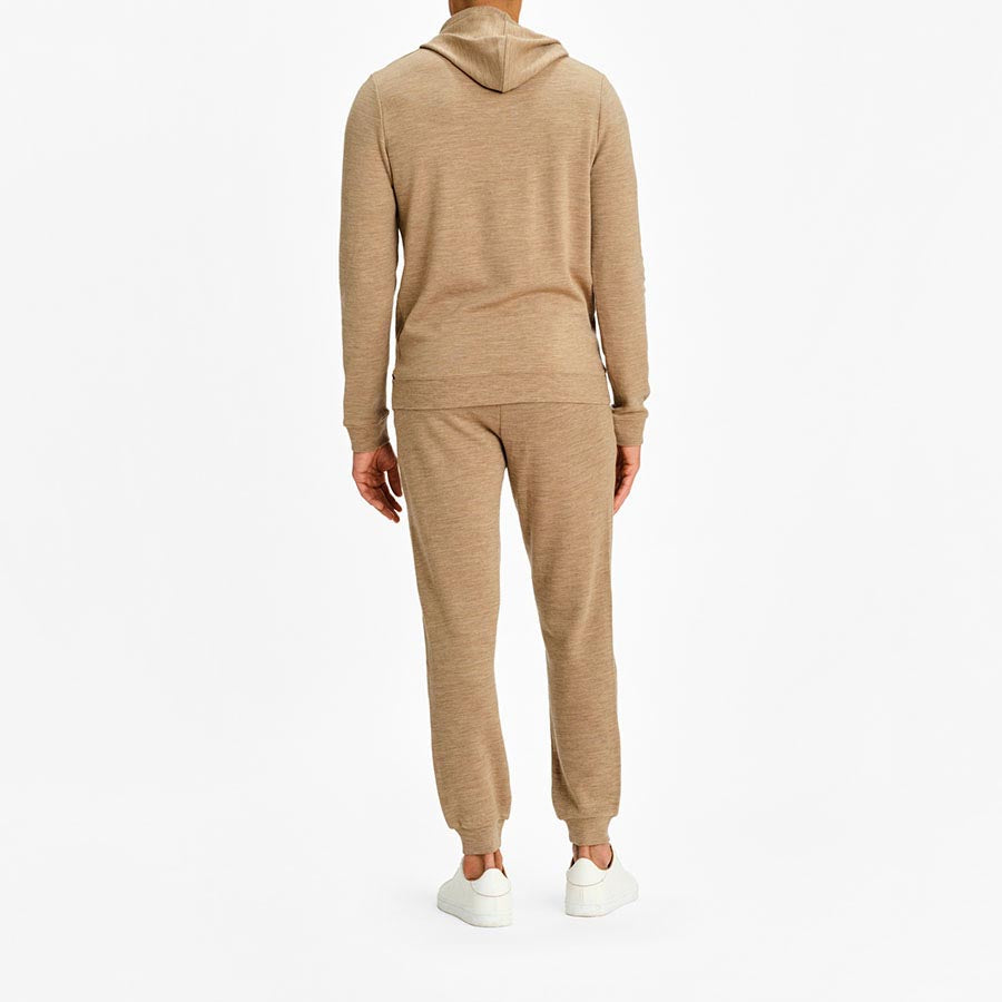 A person wearing the Tind Hoodie Men Camel by We Norwegians, crafted from breathable and antibacterial Italian Yarn, along with matching beige jogger pants, stands facing away from the camera. They are also wearing white sneakers. The background is plain and white.