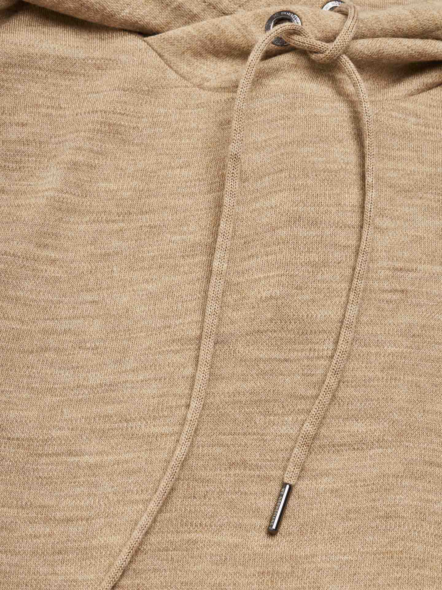 Close-up of the Tind Hoodie Men Camel by We Norwegians, showcasing its soft texture made from breathable and antibacterial Superfine Merino fabric. The beige hooded sweatshirt features drawstrings with silver metal aglets threaded through metal eyelets at the neckline, and the fabric has a slightly heathered appearance.