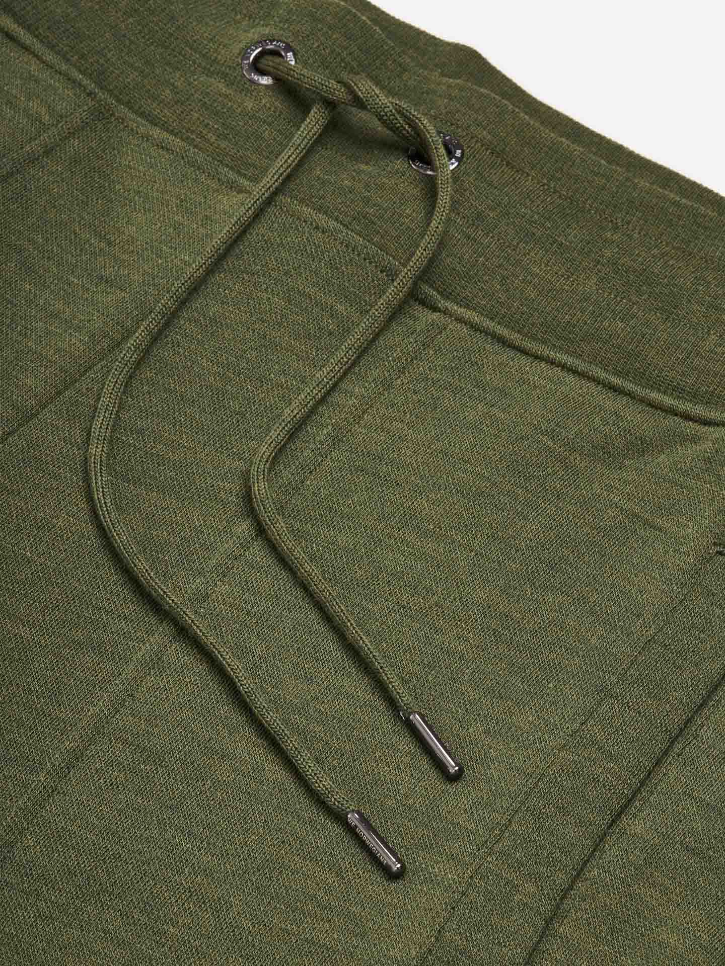 Close-up image of the Tind Joggers Men Olive Green by We Norwegians, featuring a relaxed fit with a textured fabric and drawstring tie. The drawstring sports metal aglets at the ends, and the eyelets are reinforced with metal grommets.