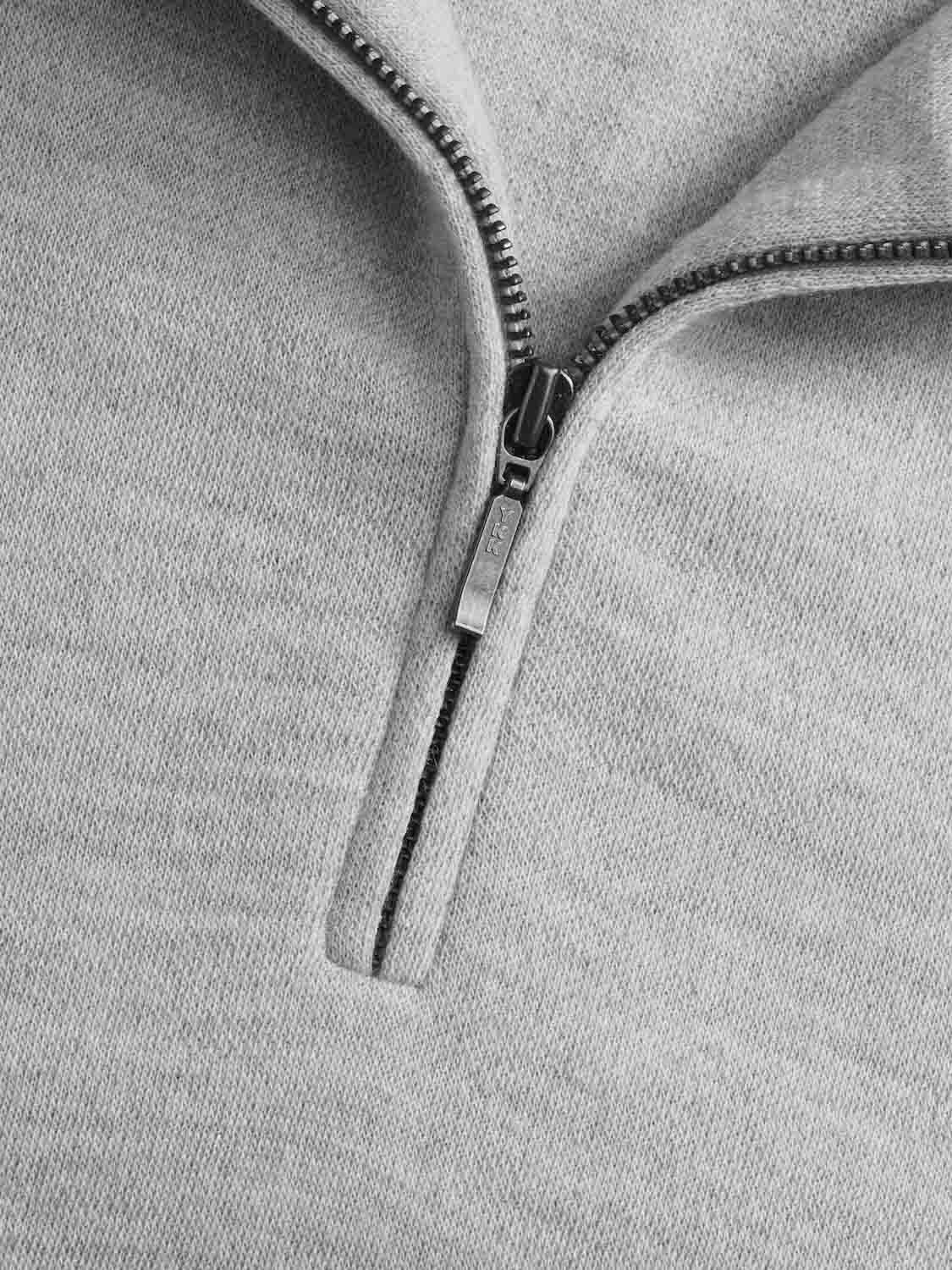 Close-up of a We Norwegians Tind 1/4 Zip Sweater Men Grey Melange. The image focuses on the partially unzipped, metallic zipper, offering a detailed view of the zipper teeth and the fabric. Crafted from superfine Merino wool, the fabric showcases a soft, slightly textured appearance.