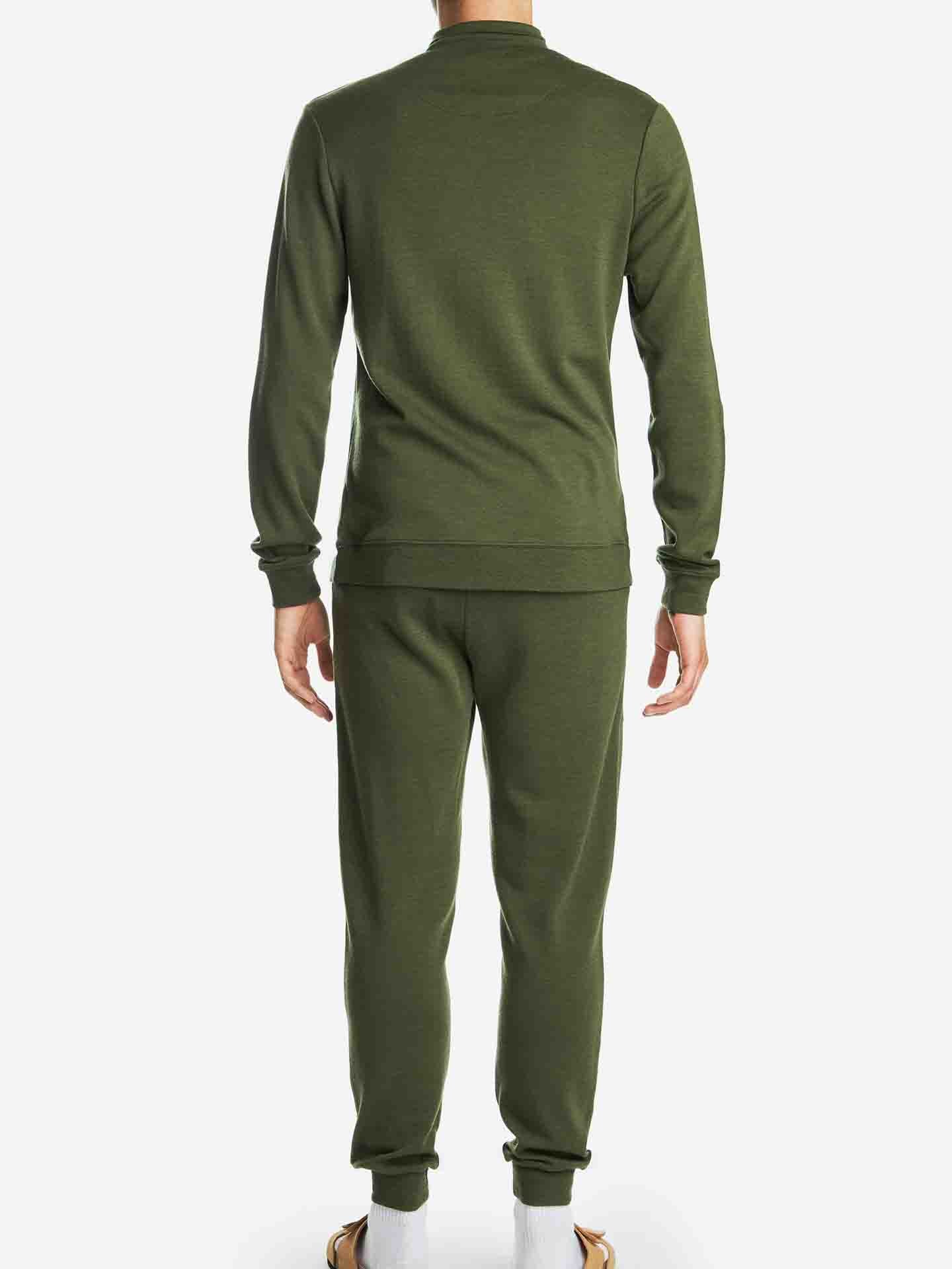 A person is seen from the back wearing an olive green We Norwegians Tind 1/4 Zip Sweater and matching pants, both made of structured jacquard knit. The individual is also wearing white socks and tan slip-on sandals, all set against a plain white background.