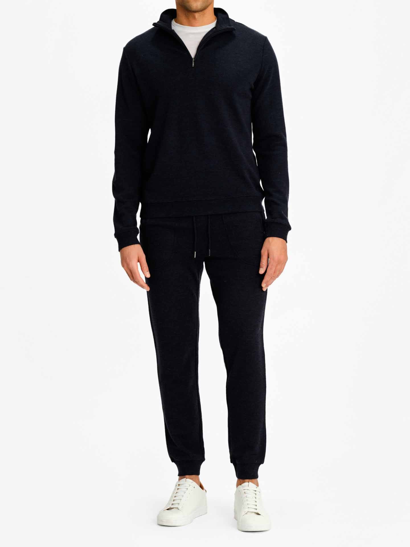 A person stands against a white background, showcasing the Limited Time Bundle: Tind 1/4 Zip & Tind Joggers Men from Fast Bundle—a matching black zip-up pullover and jogger pants with a t-shirt underneath. The outfit is completed with white casual sneakers. The person's head is not visible in the image, highlighting the contemporary designs of the ensemble.