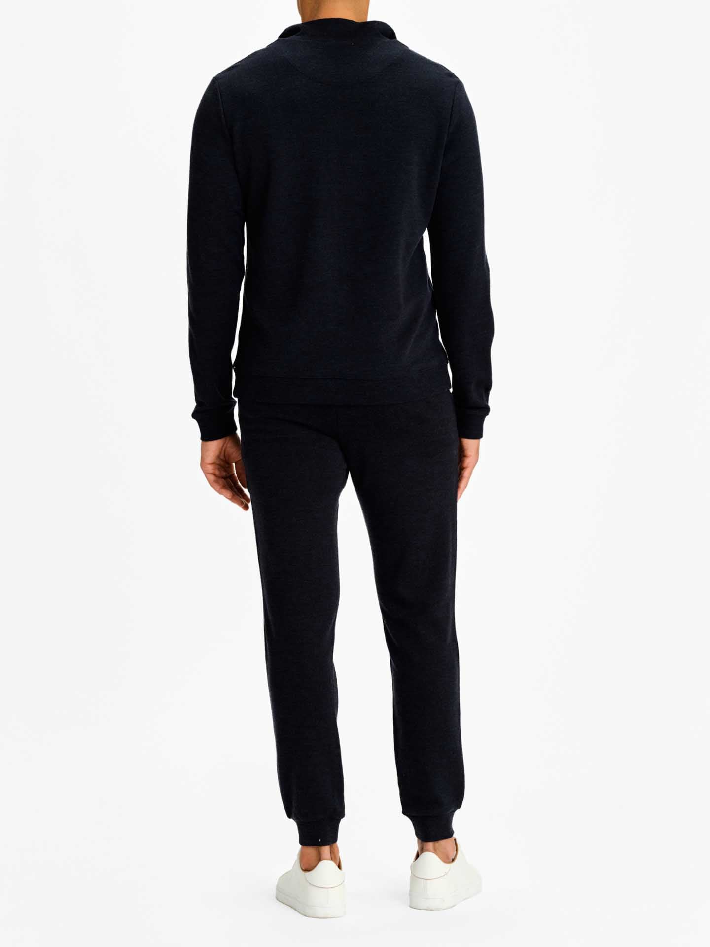 Rear view of a person wearing a navy 1/4 zip sweater and black jogger pants with white sneakers, standing against a white background, showcasing the sleek elegance of We Norwegians' Tind products.